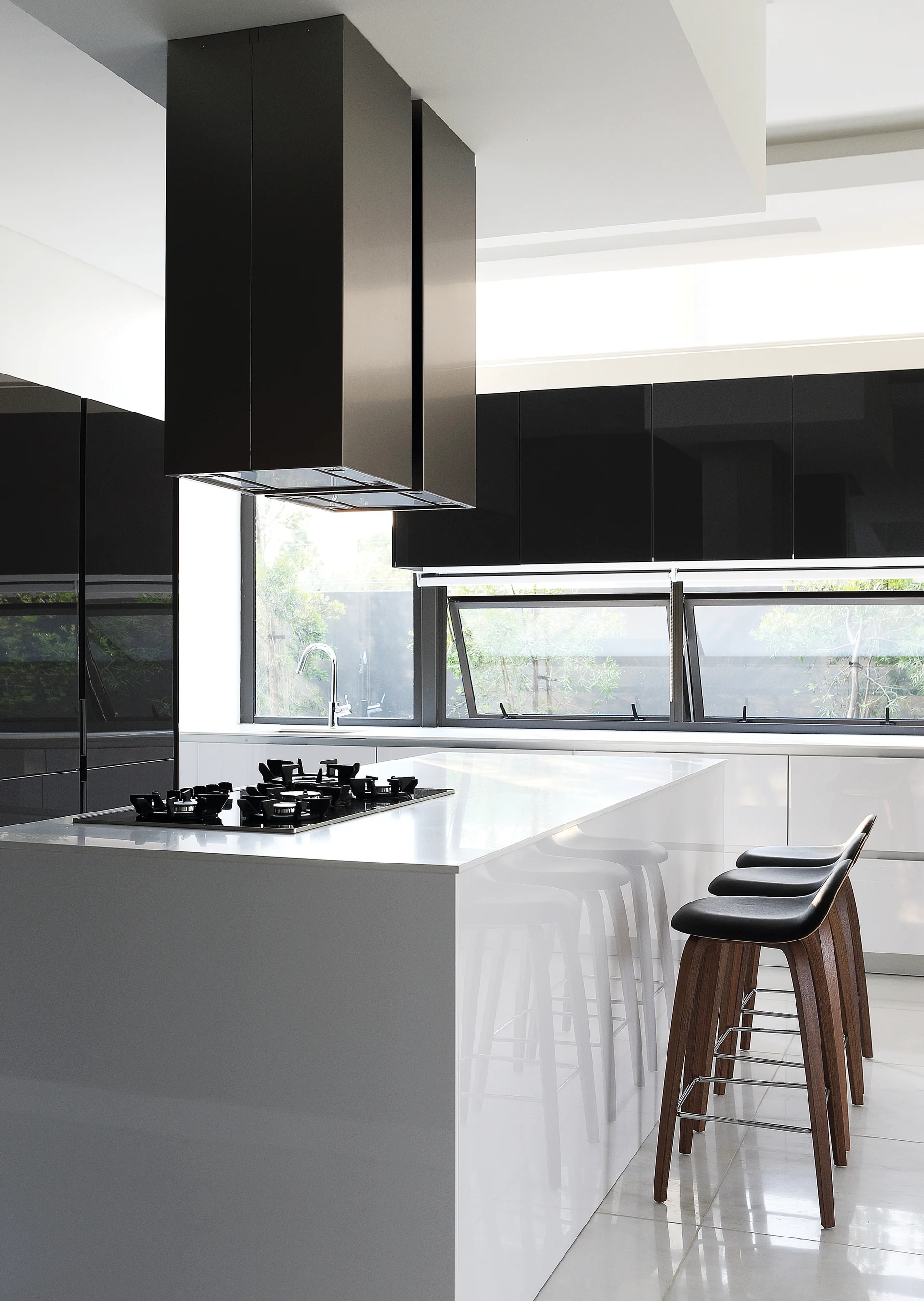 A modern kitchen featuring a glossy white island with a built-in cooktop, high-gloss black upper cabinets, and dark wood bar stools.