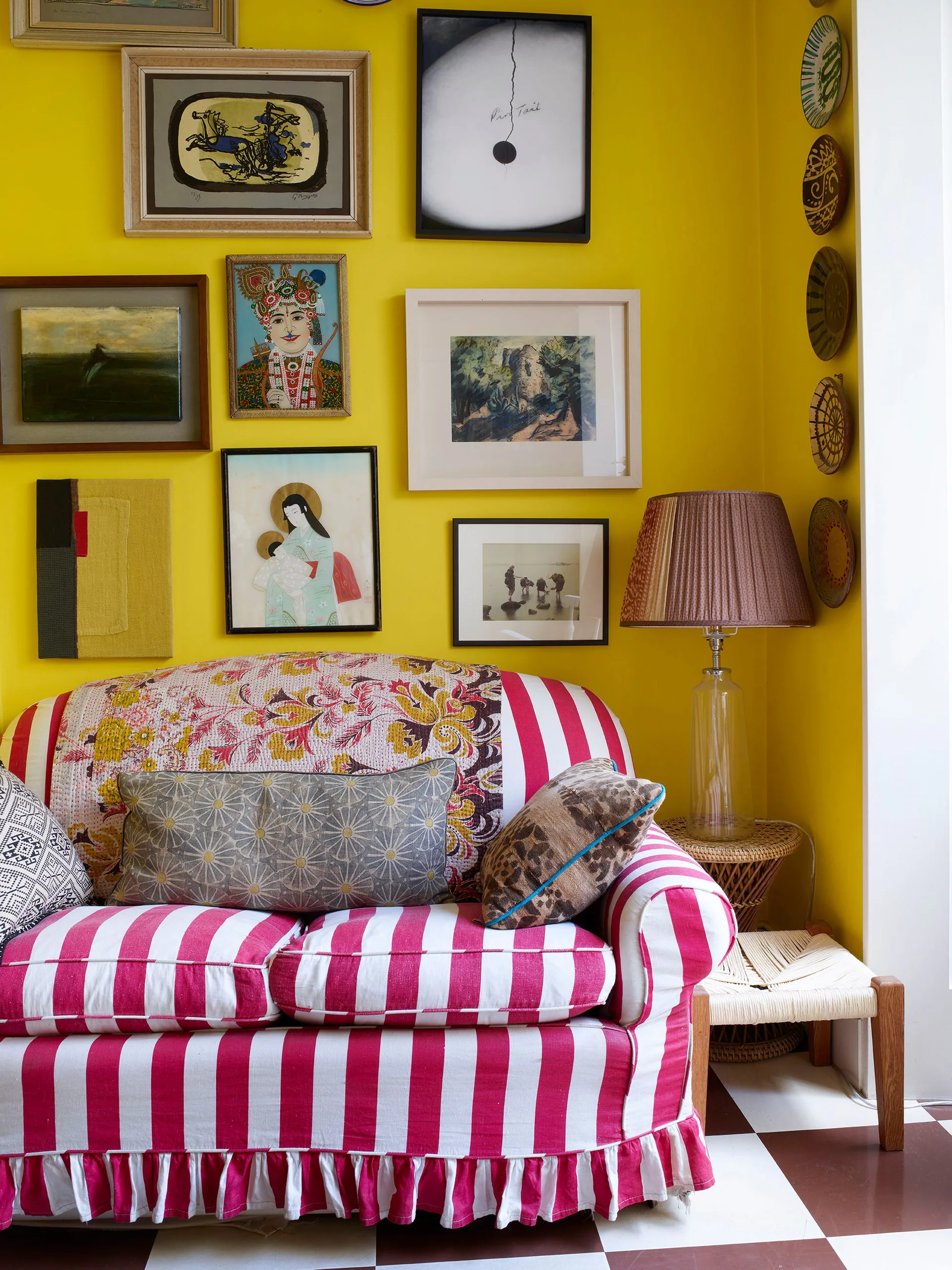A pink and white striped sofa sits against a bright yellow wall decorated with a gallery of framed art.