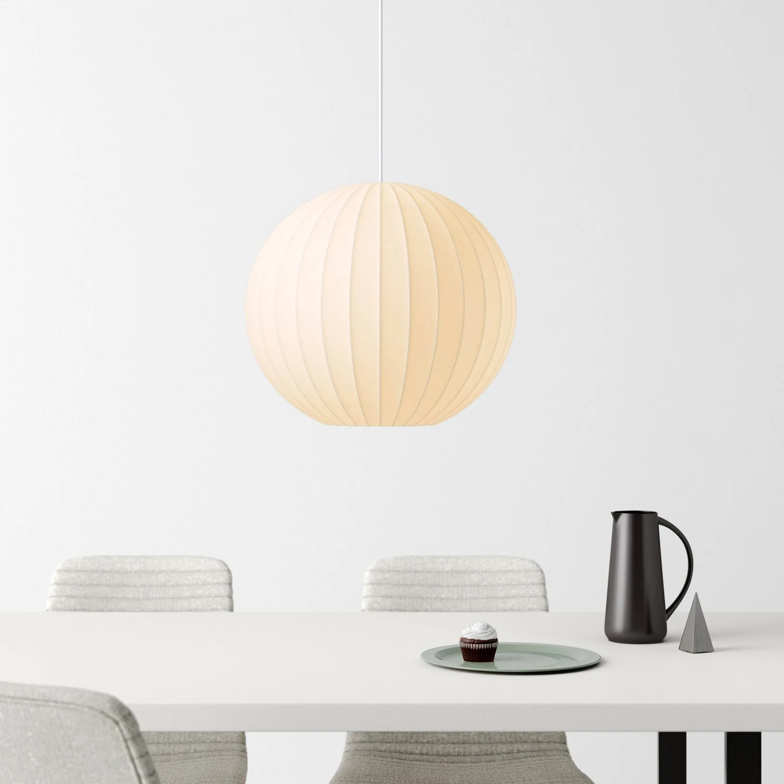 A ribbed spherical pendant light hangs over a minimalist white dining table set with light grey upholstered chairs and a few dark decor objects.