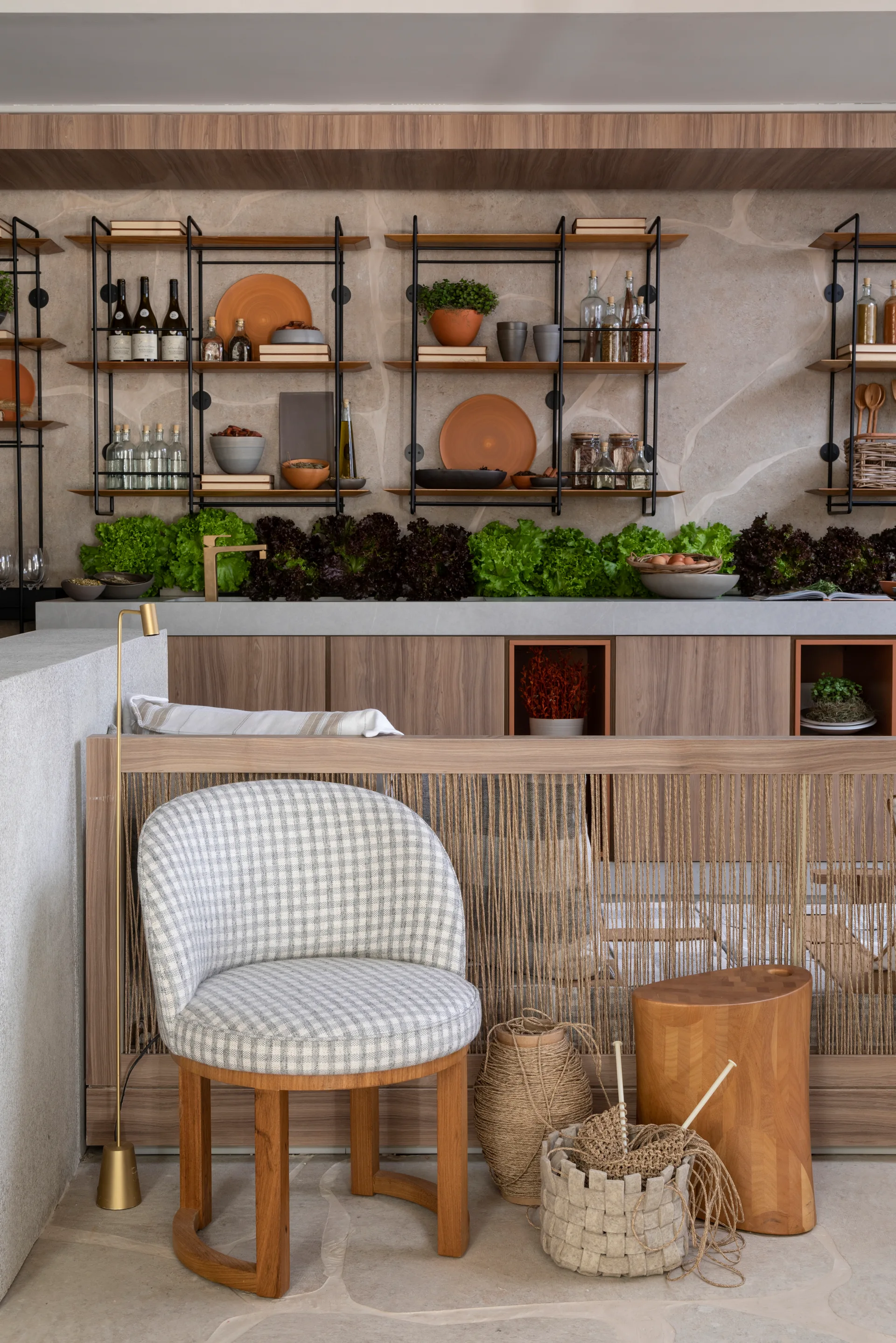 An organic modern kitchen features a textured stone wall, open metal shelves, wood cabinetry, and a plaid upholstered accent chair.