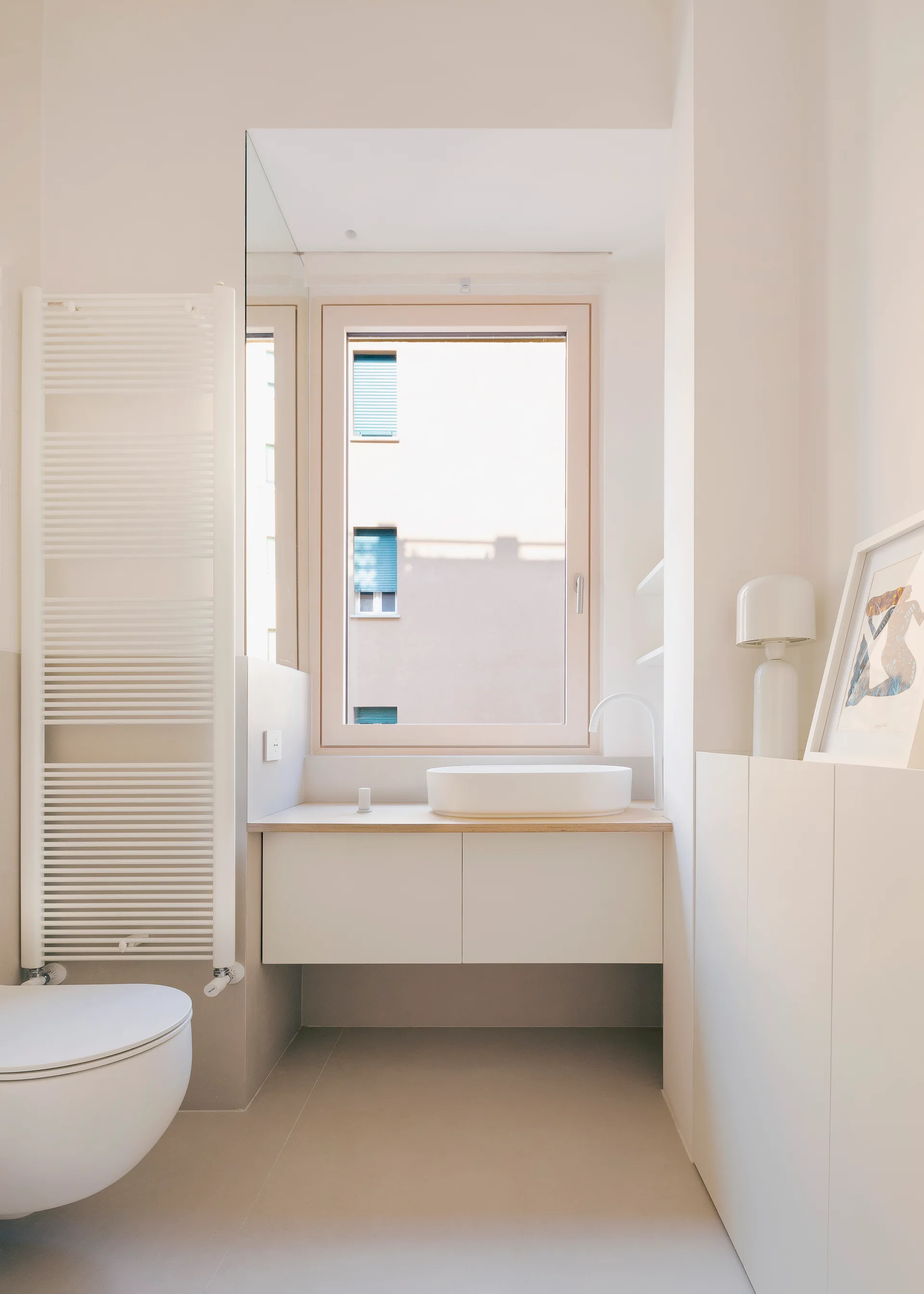A minimalist off-white bathroom features a floating vanity with a round vessel sink under a window, next to a white ladder towel radiator.