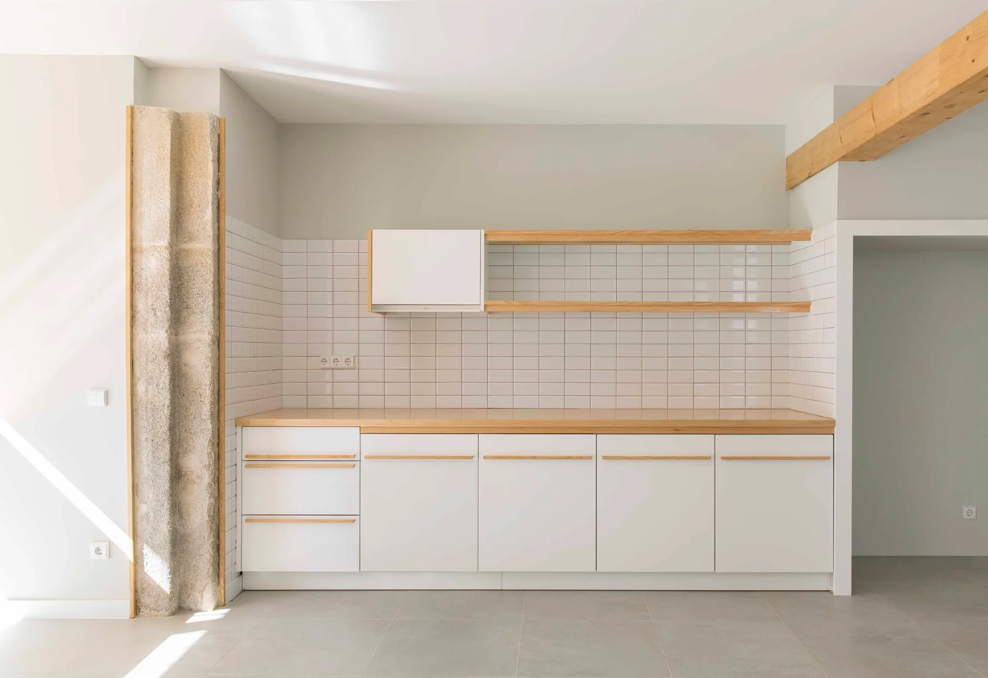 Minimalist kitchen featuring white base cabinets with light wood trim, a matching wood countertop, floating shelves, and a square white tile backsplash.