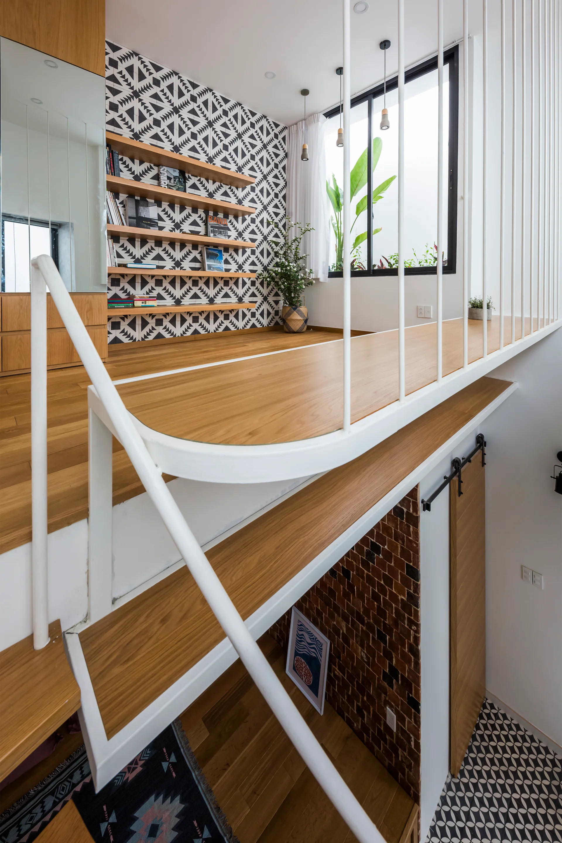 A wood-floored mezzanine landing features a white metal vertical railing, floating wooden shelves, and a black and white geometric patterned wall.
