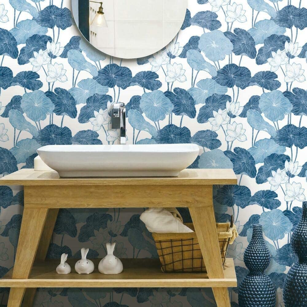 A light wood console vanity with a white vessel sink stands against a blue and white floral patterned wallpaper.