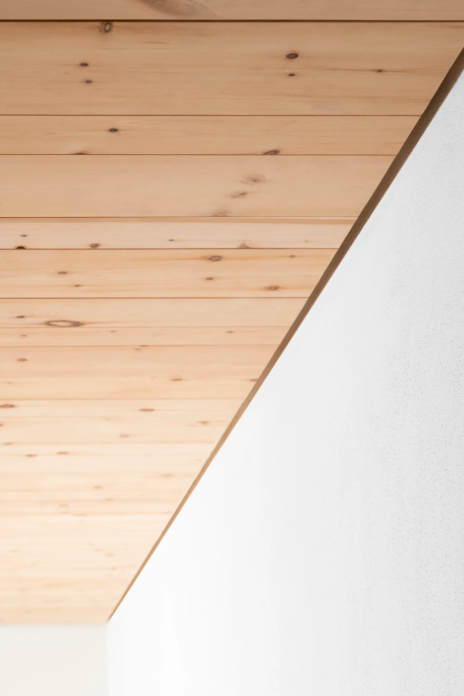 A close-up view shows natural light wood ceiling planks meeting a smooth white wall with a clean shadow gap.