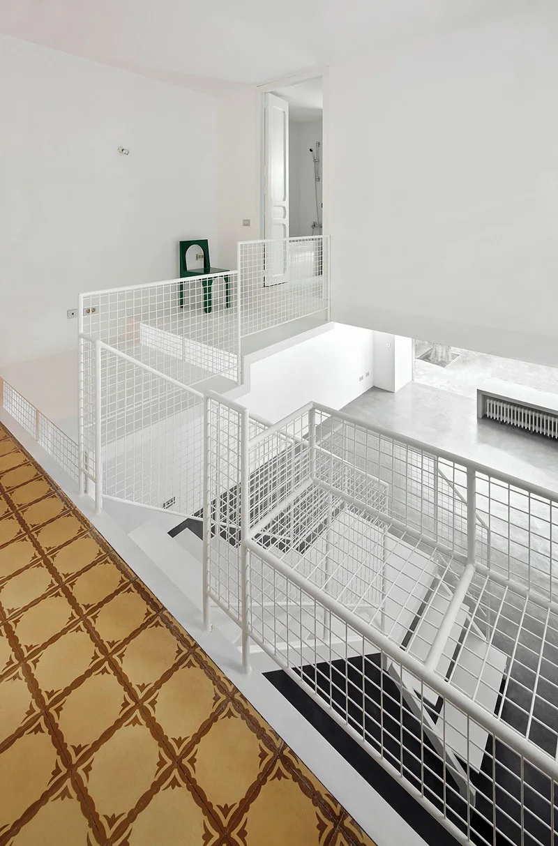 A modern staircase with white wire mesh railings sits next to patterned yellow floor tiles and a green accent chair on the landing.