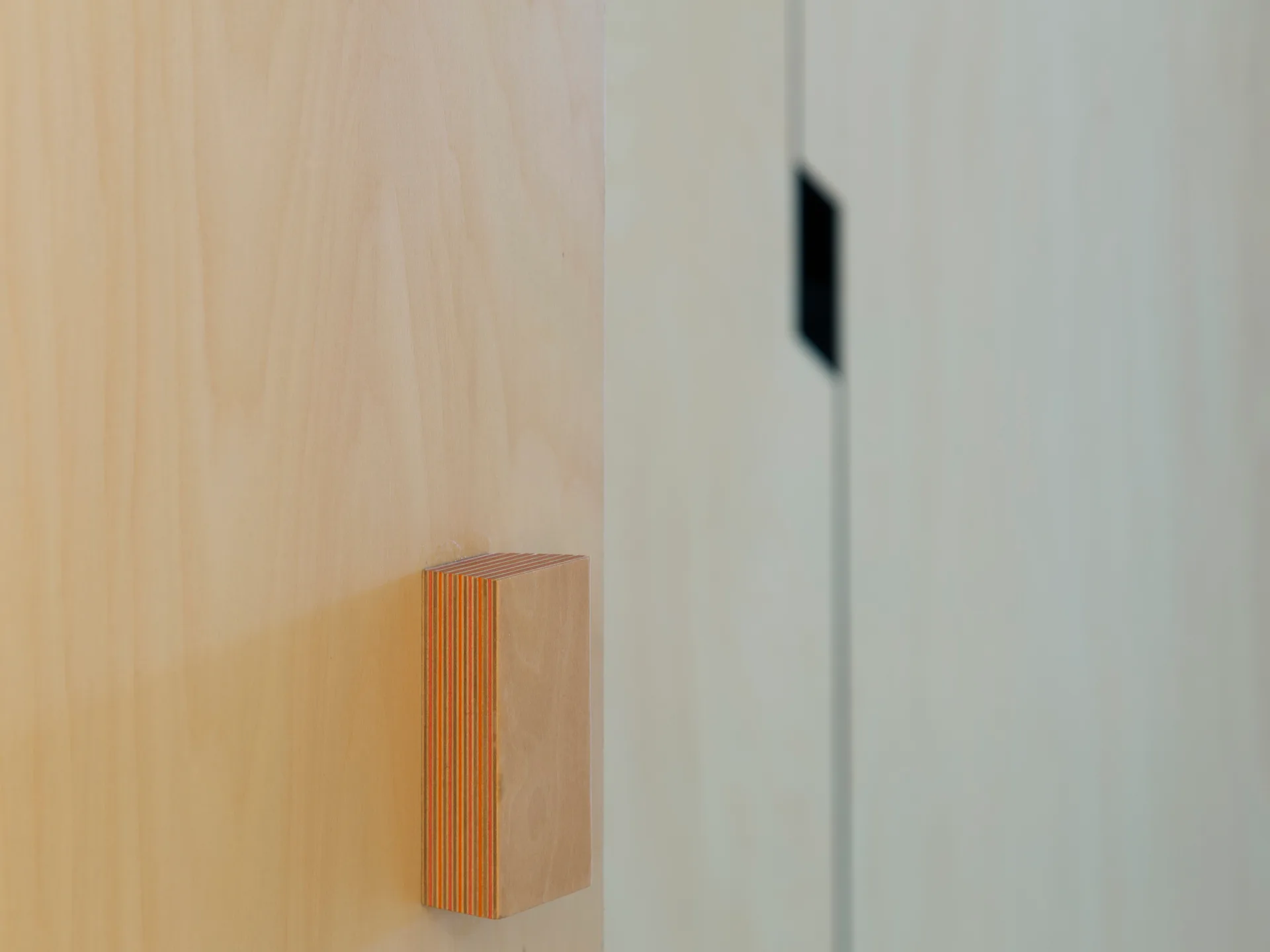 A close-up of a light wood cabinet door featuring a custom rectangular handle with visible layered plywood edges.