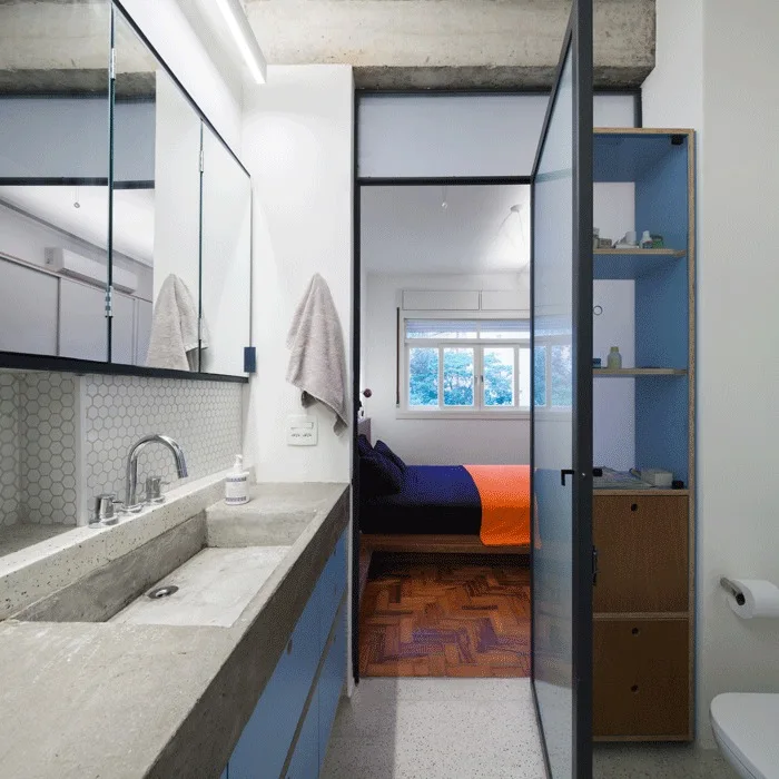 A bathroom featuring a concrete integrated sink and blue cabinetry next to a glass door opening into a bedroom with parquet flooring.