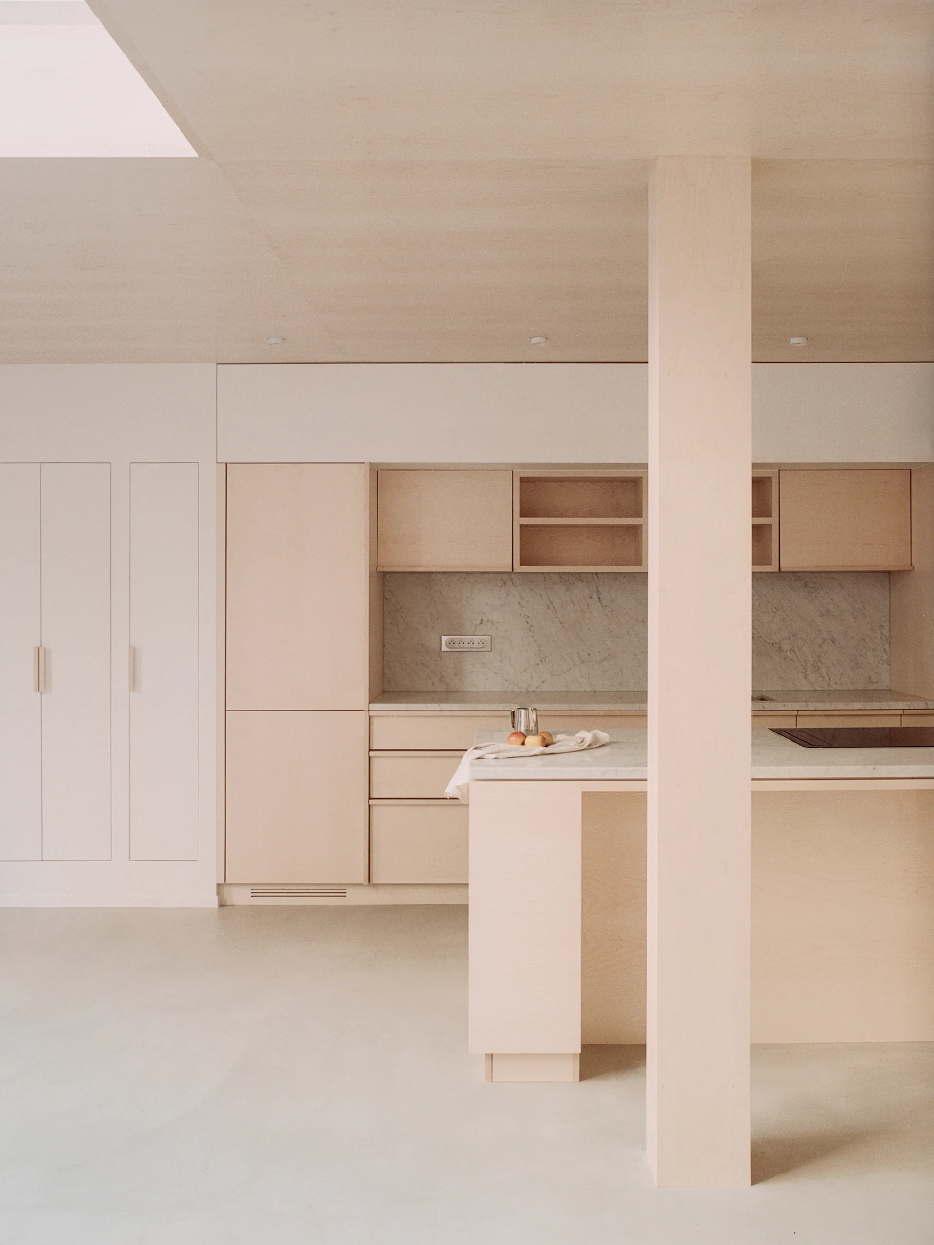 A minimalist kitchen features light wood flat-panel cabinetry, a marble backsplash, and a matching kitchen island under a wood-clad ceiling.