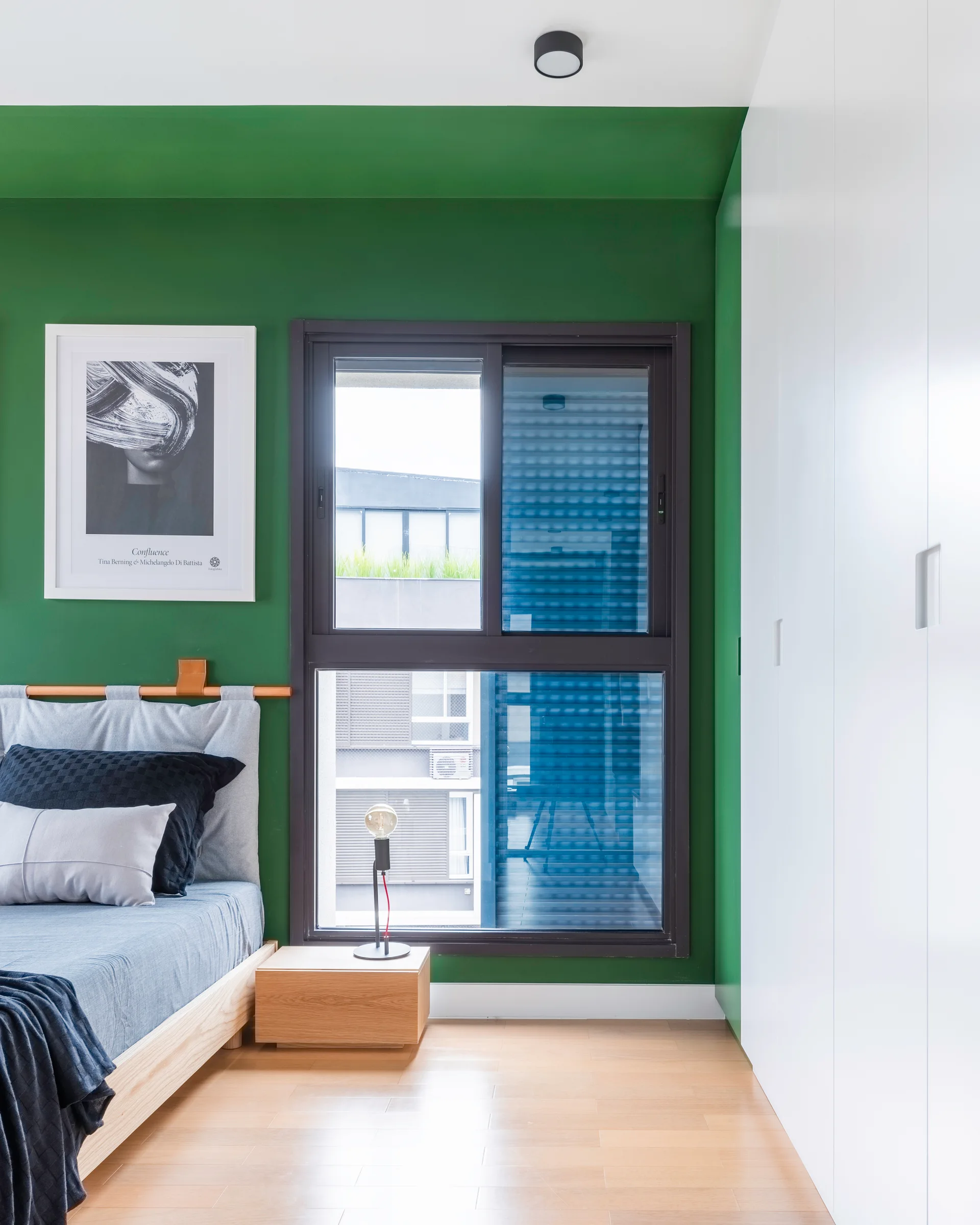 A modern bedroom featuring a bold green accent wall, a light wood platform bed with a gray headboard, and sleek white wardrobes.