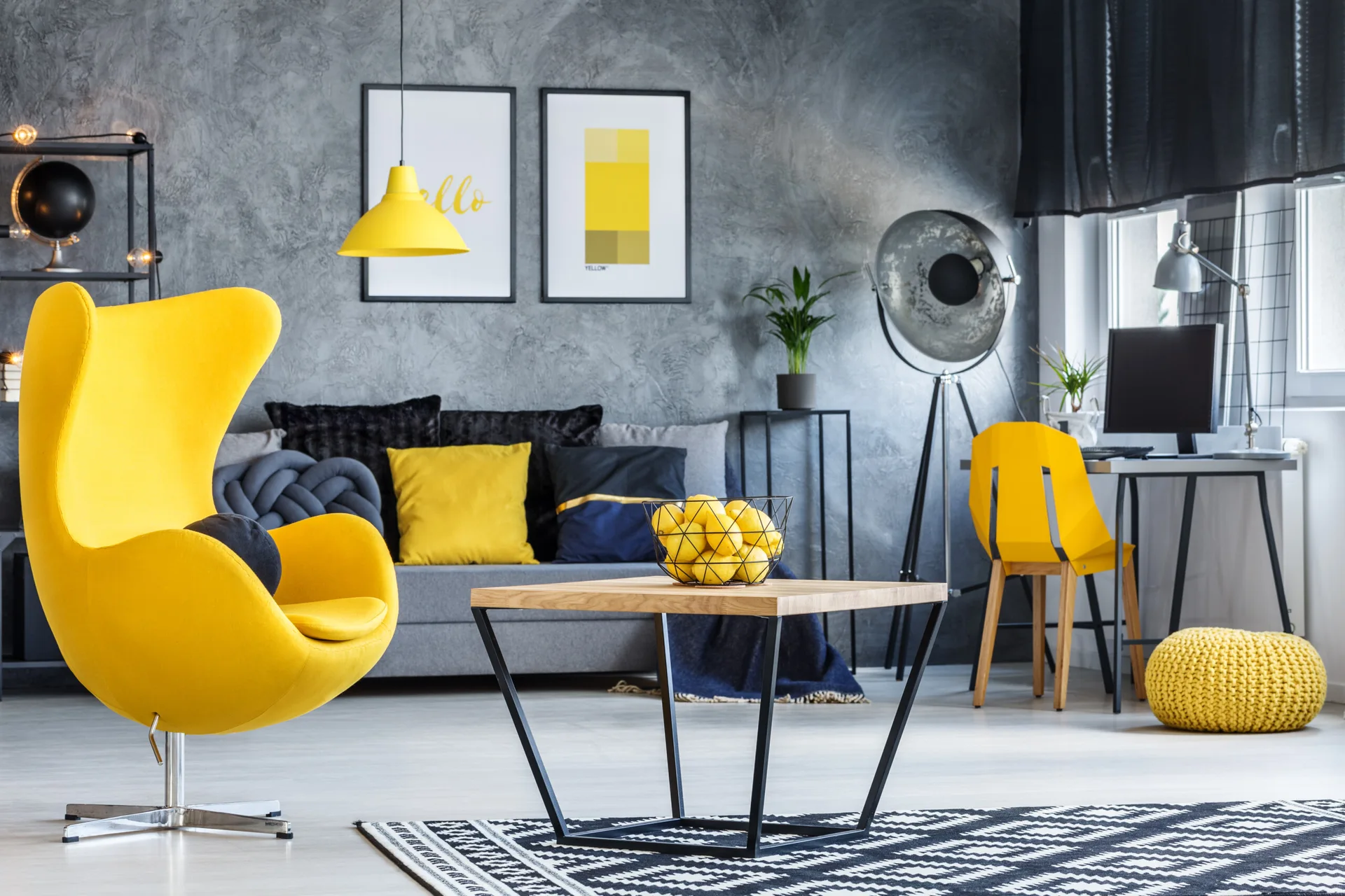 A modern living room features a textured grey wall, a bright yellow egg chair, a grey sofa, and a black and white geometric rug.