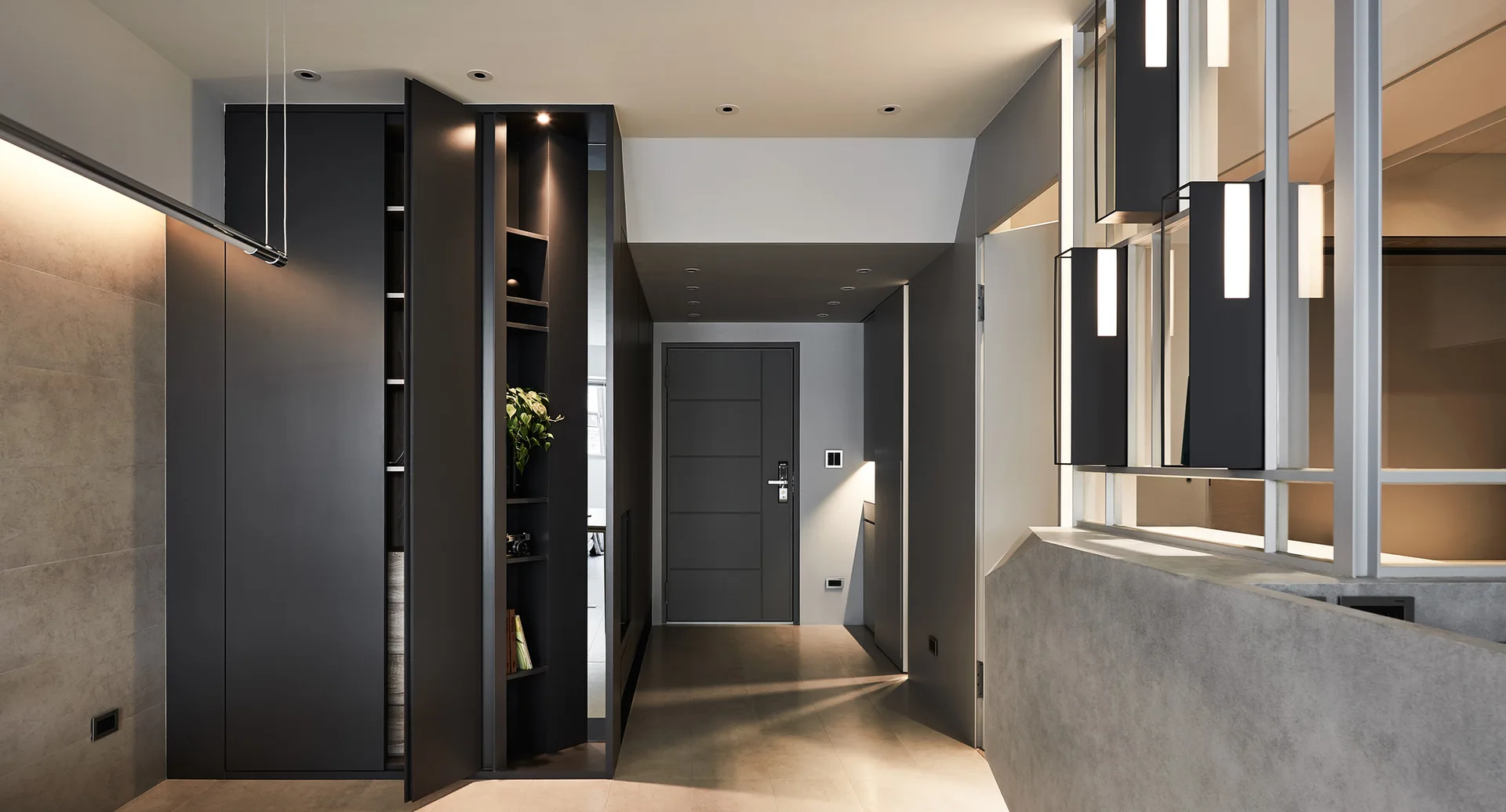 A modern entryway featuring dark matte cabinetry, integrated lighting, a gray entry door, and a concrete half wall with a glass partition.