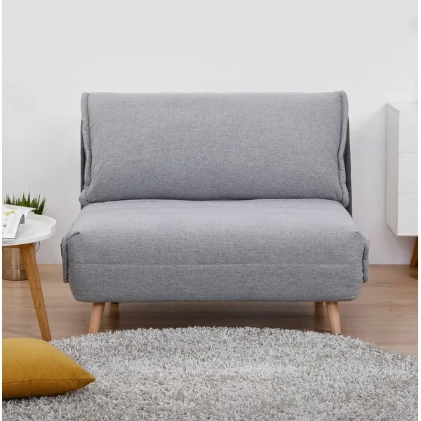 A gray armless convertible sleeper chair on a light wood floor near a gray shag rug and a white side table.