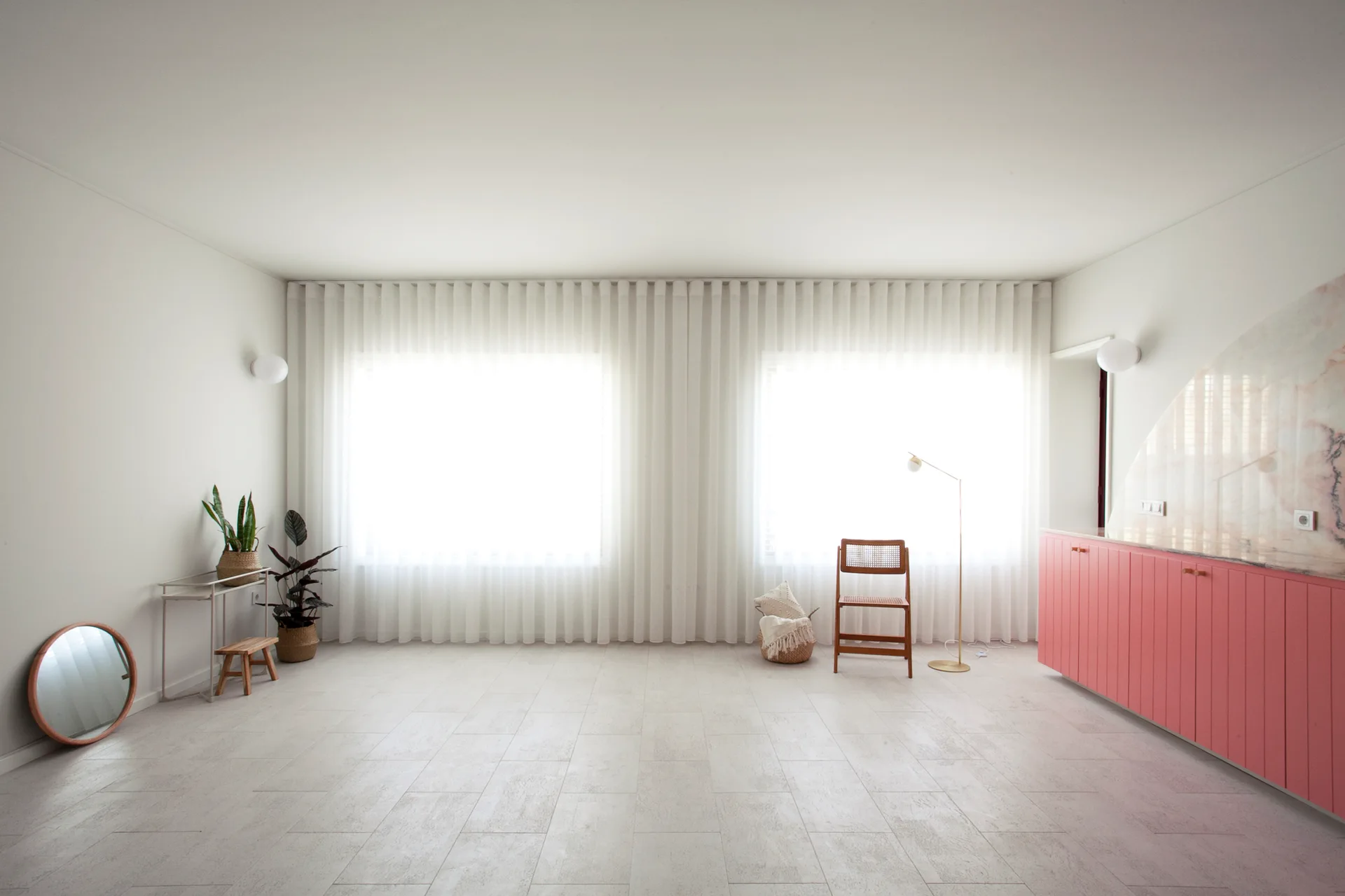 A minimalist bedroom featuring light tile flooring, sheer white drapes along the back wall, and low pink cabinetry.