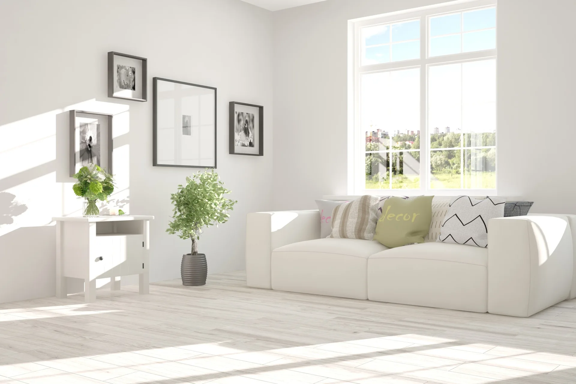 Bright minimalist living room featuring a white sofa with accent pillows, a large window, light wood floors, and staggered framed artwork on the wall.