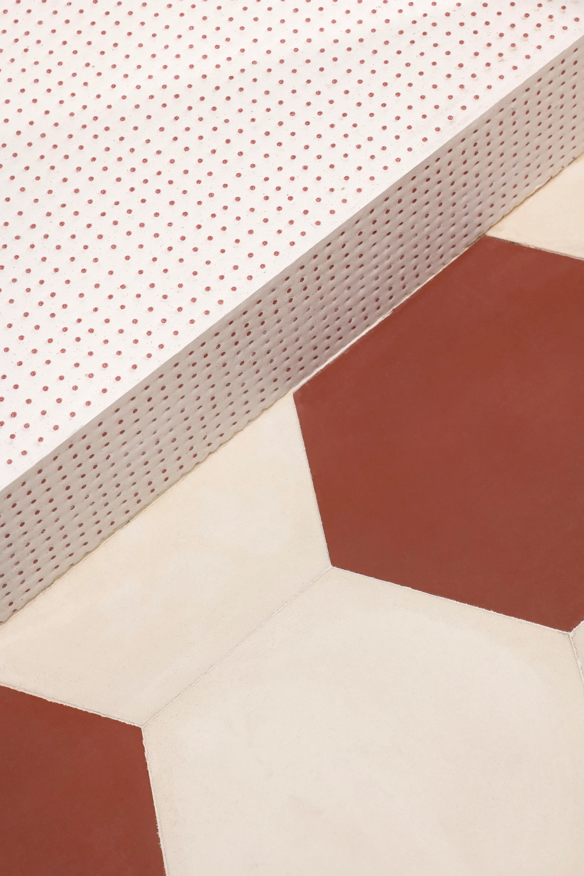 A close-up of a white perforated panel with small red dots resting on hexagonal terracotta and beige floor tiles.