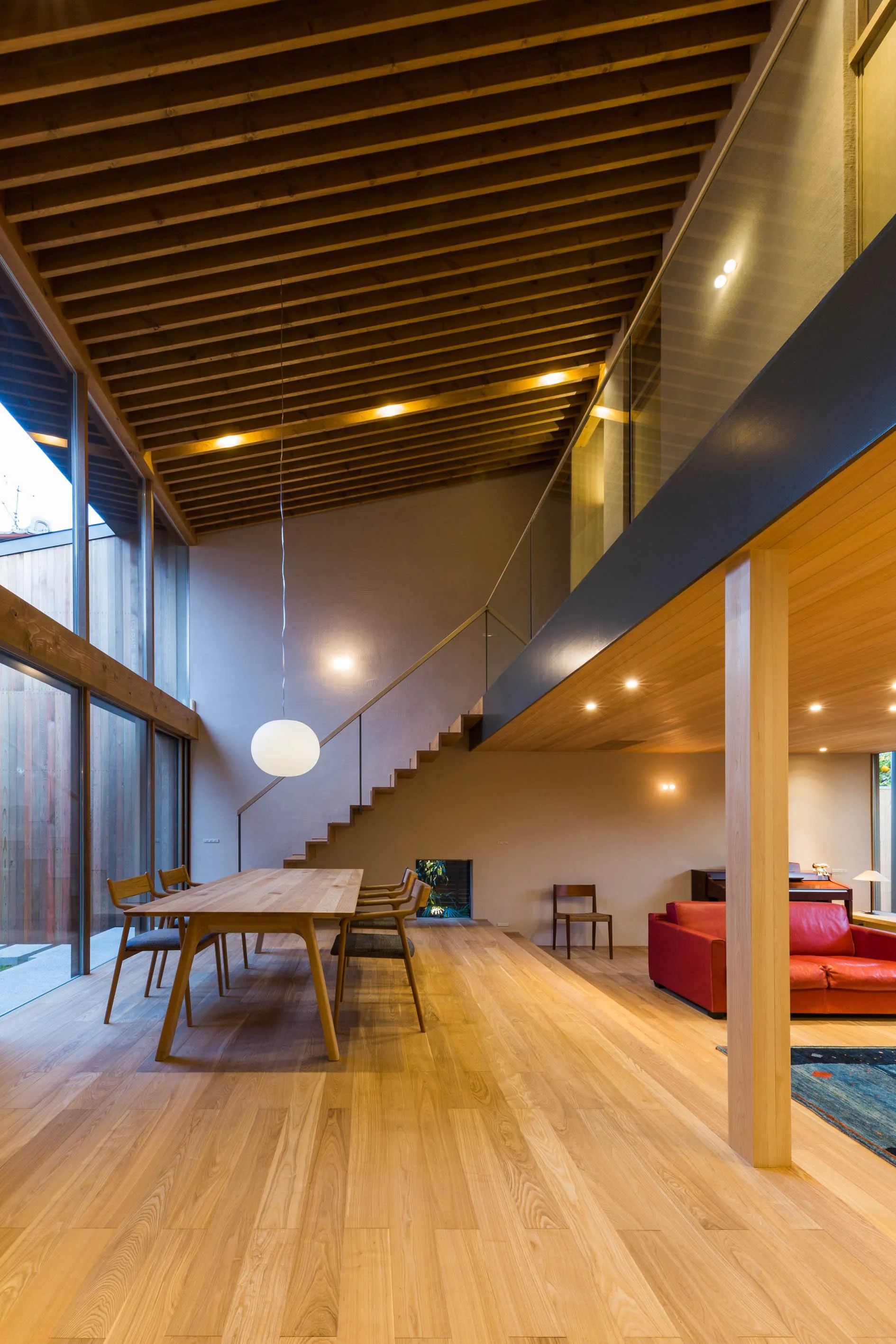 A modern open dining room with a large wooden table and chairs sits beneath a dramatic sloped ceiling with exposed timber rafters.