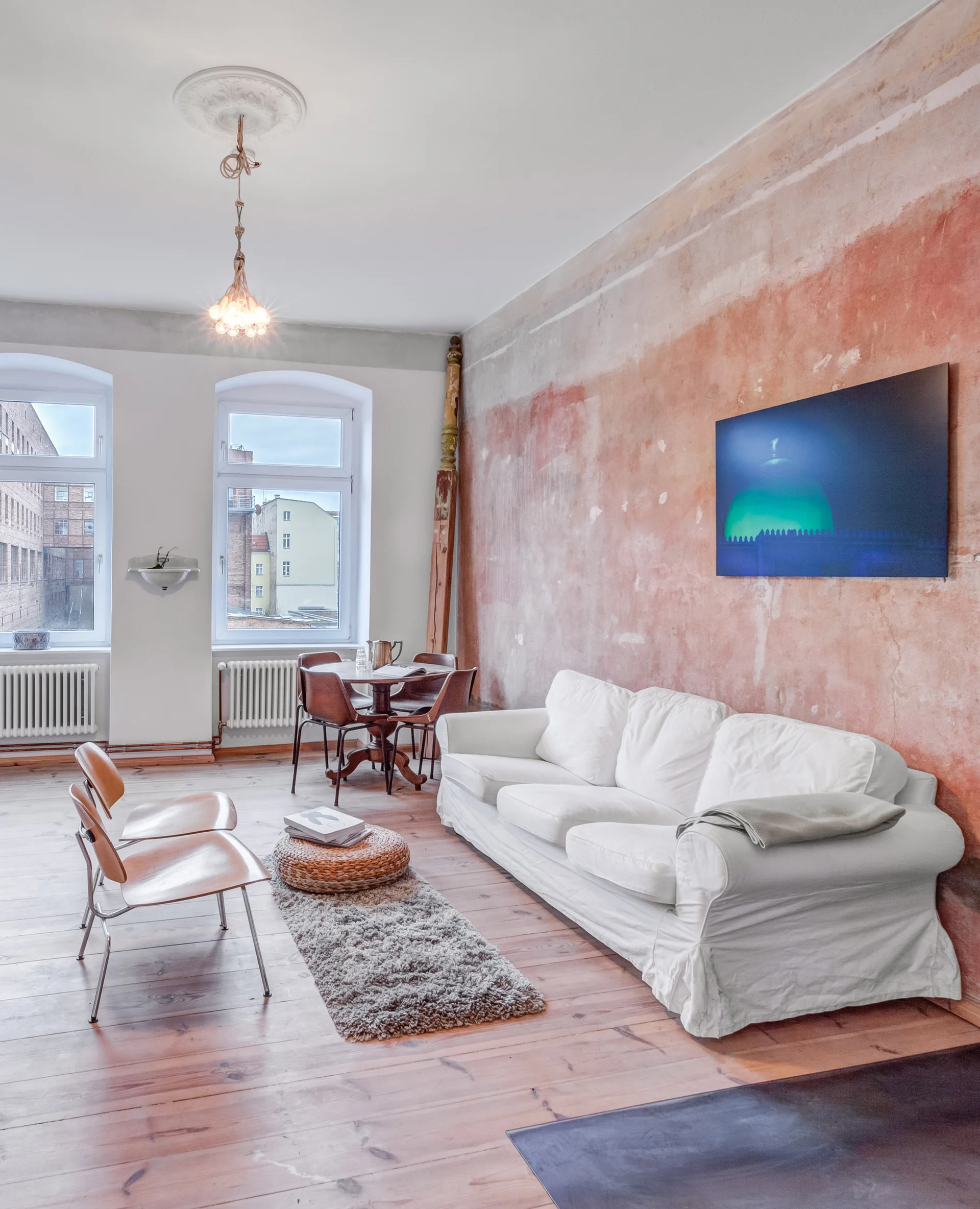 A spacious living room features a white slipcovered sofa set against a raw, textured terracotta plaster wall with a blue modern painting.