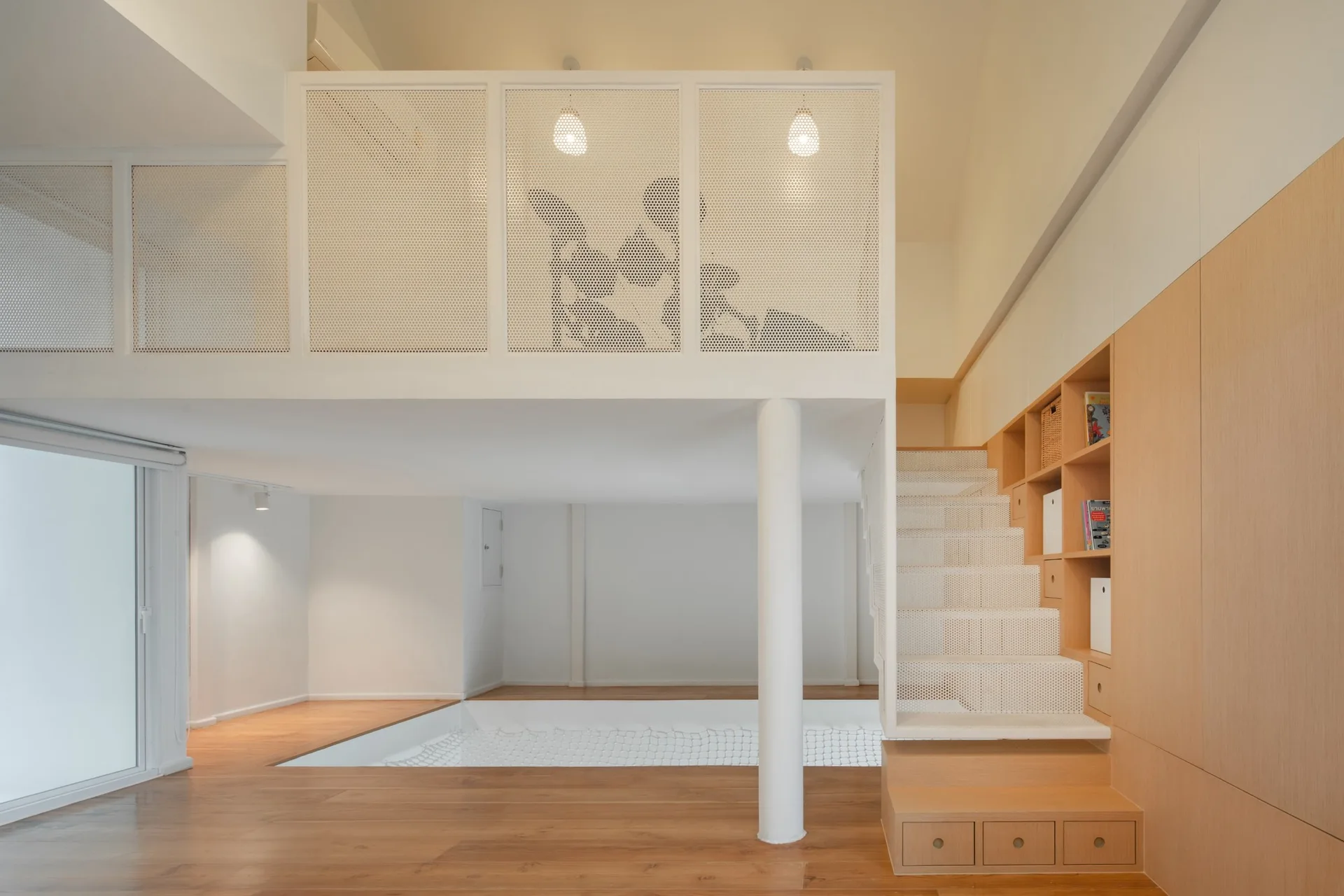 A modern mezzanine loft features a white perforated metal railing, light wood floors, and a wooden staircase with integrated storage shelving.