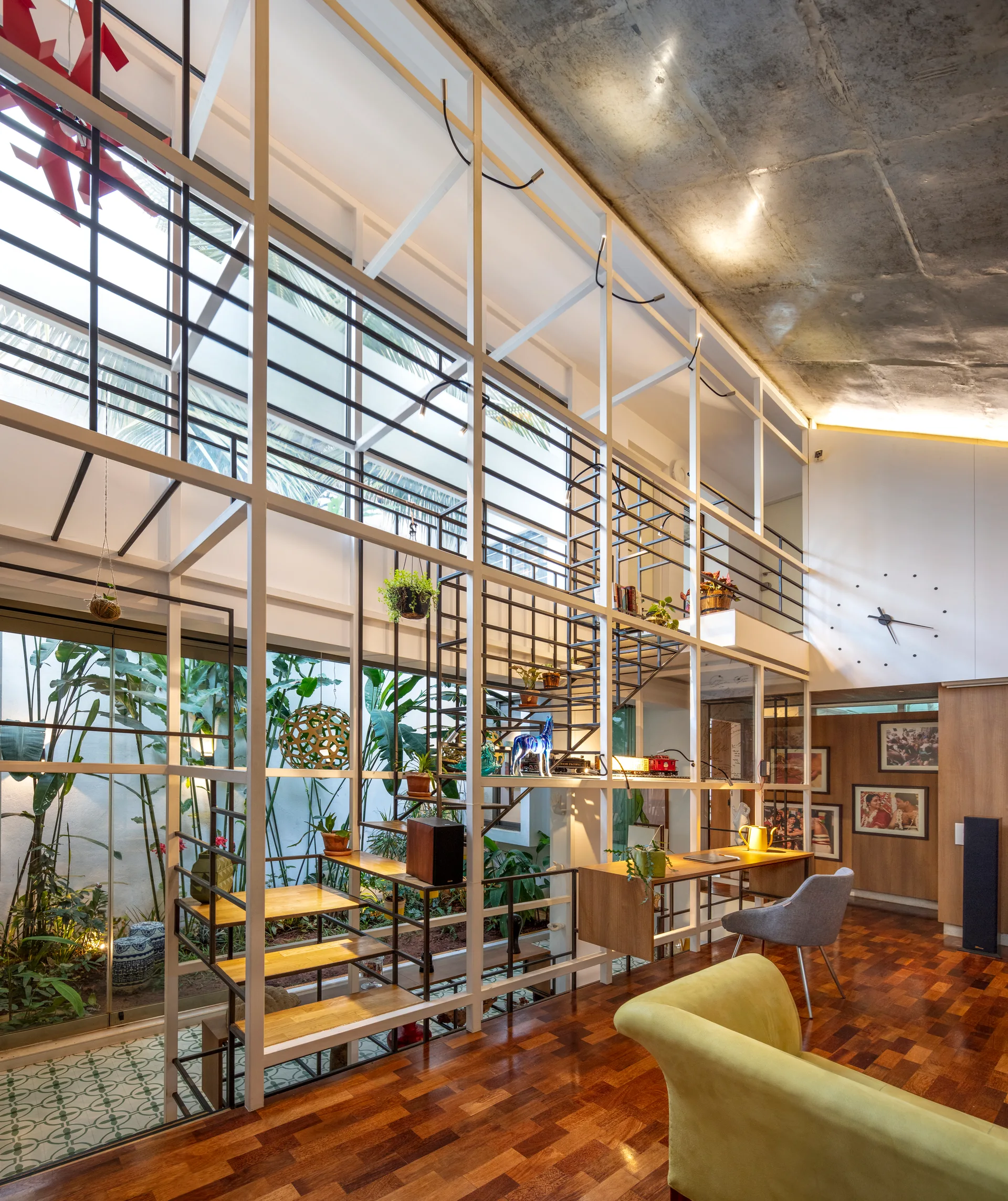 A contemporary living room featuring a floor-to-ceiling white metal structural grid that integrates a floating wooden desk and open stairs.