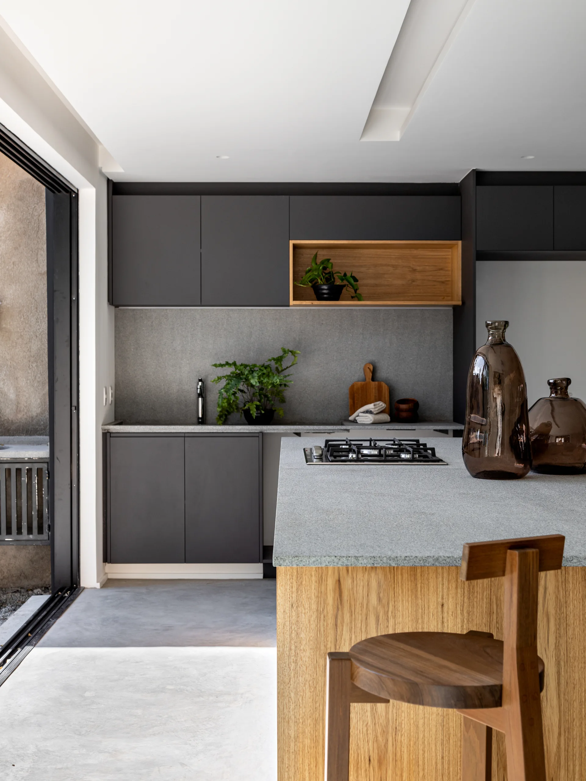 A modern kitchen featuring charcoal grey cabinets, a natural wood island with a gas cooktop, and speckled grey stone countertops.