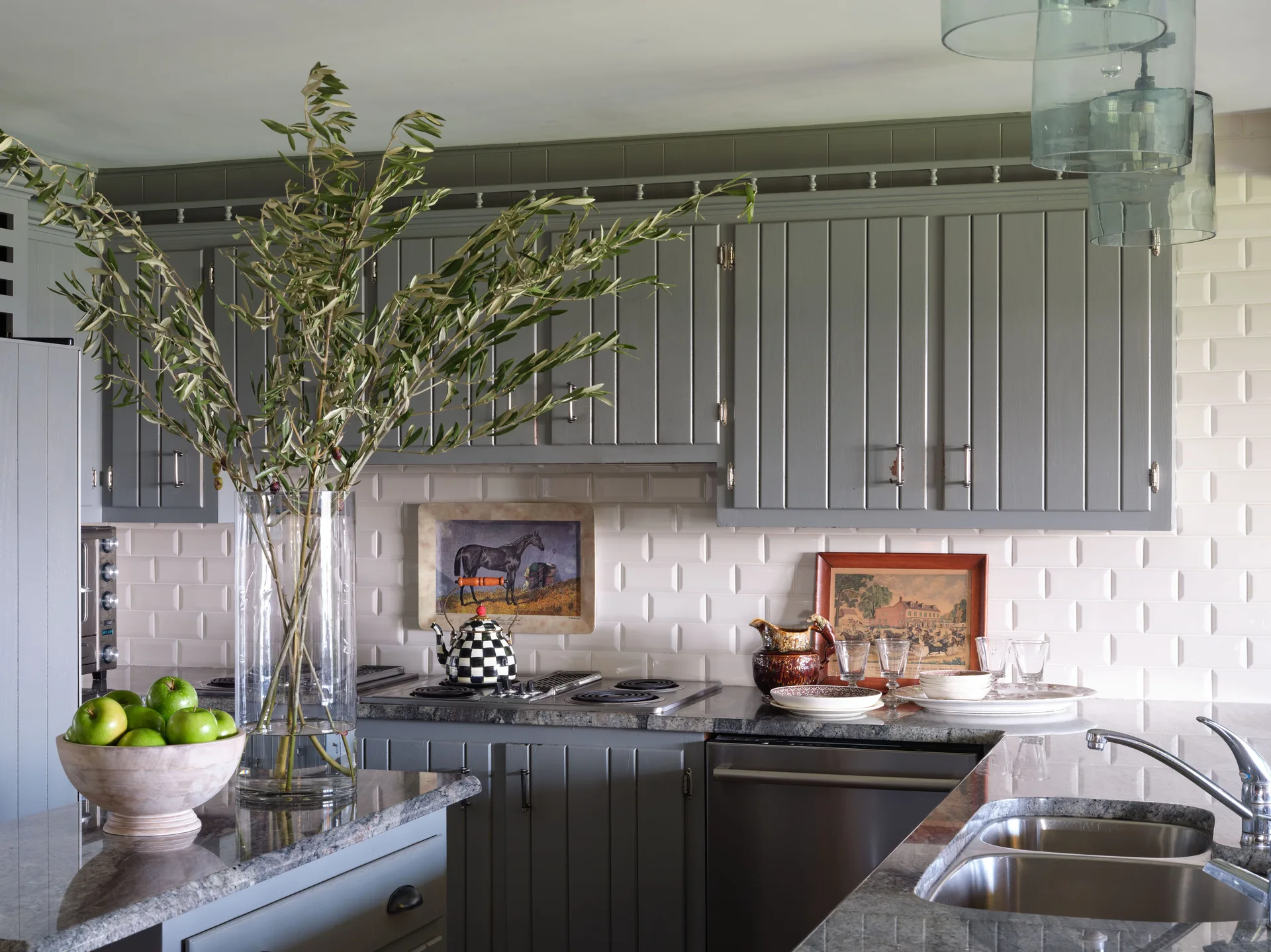 Grey vertical-panel kitchen cabinets are paired with a white subway tile backsplash, granite countertops, and a stainless steel sink.