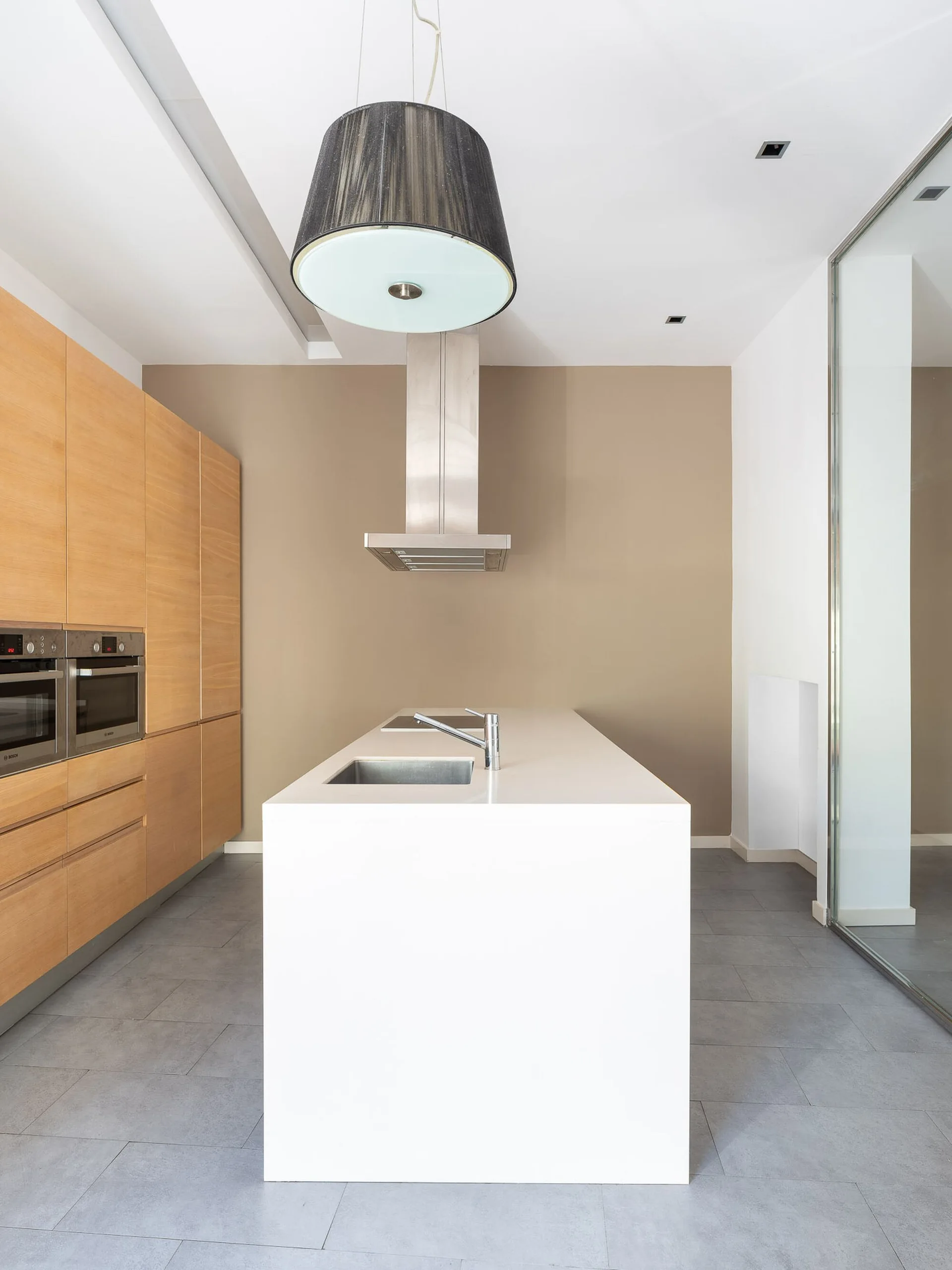 A modern kitchen features a central white island with a sink, full-height wood cabinets, a gray tiled floor, and a beige accent wall.