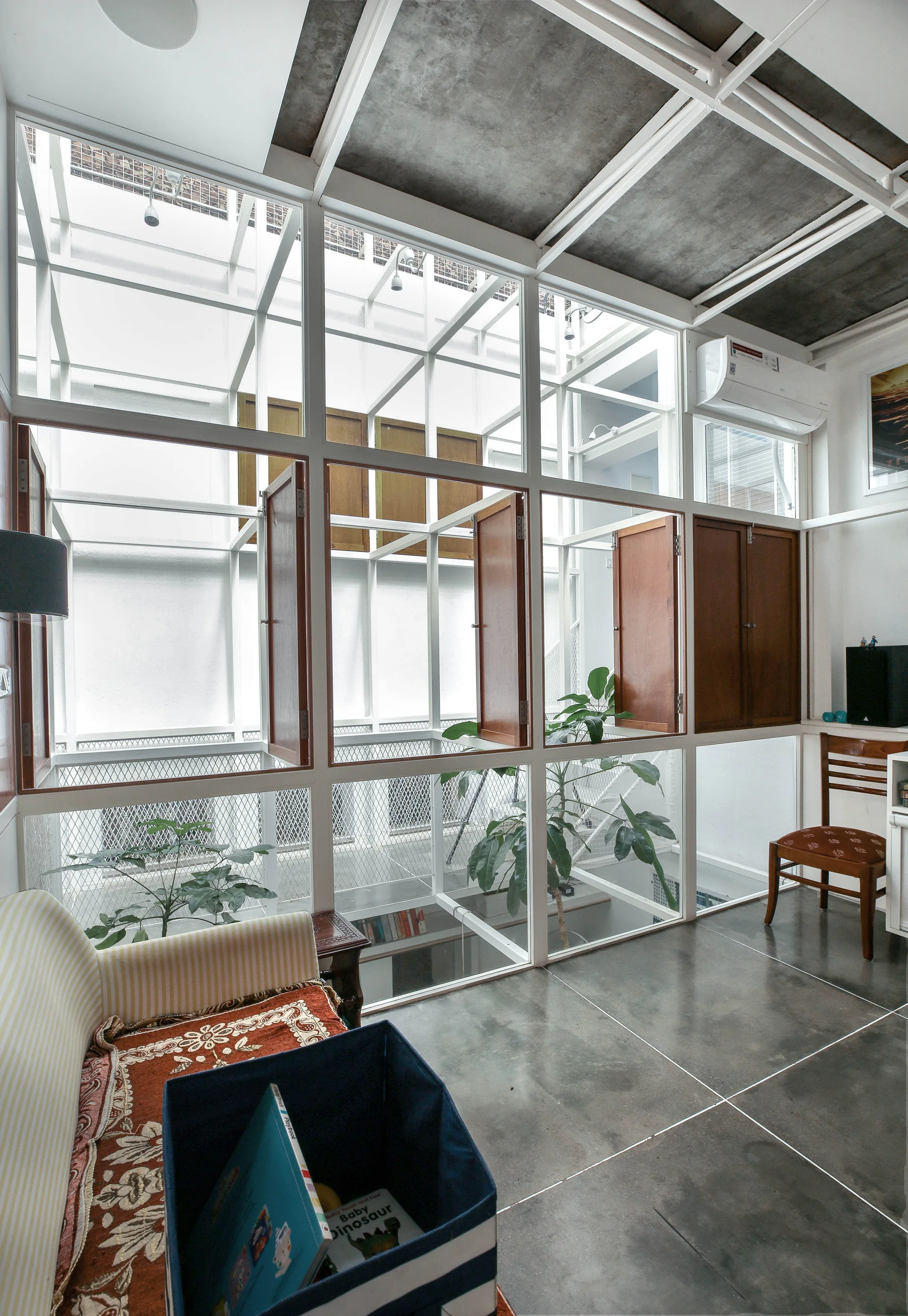 An interior living space features a large white metal grid window with built-in wooden shutters, a grey tiled floor, and a striped sofa.