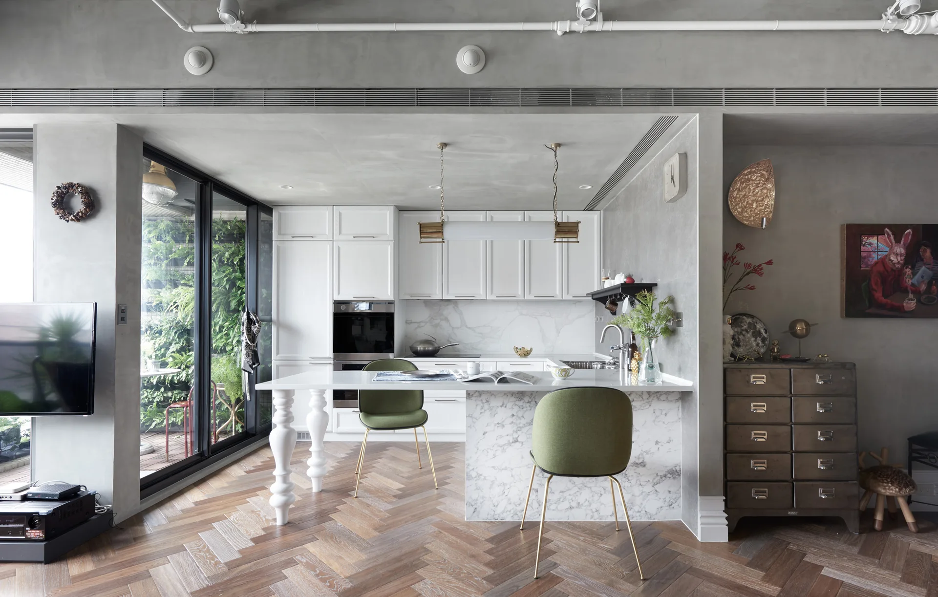 A modern kitchen featuring white cabinetry, a marble-clad island, green dining chairs, and a raw concrete ceiling.