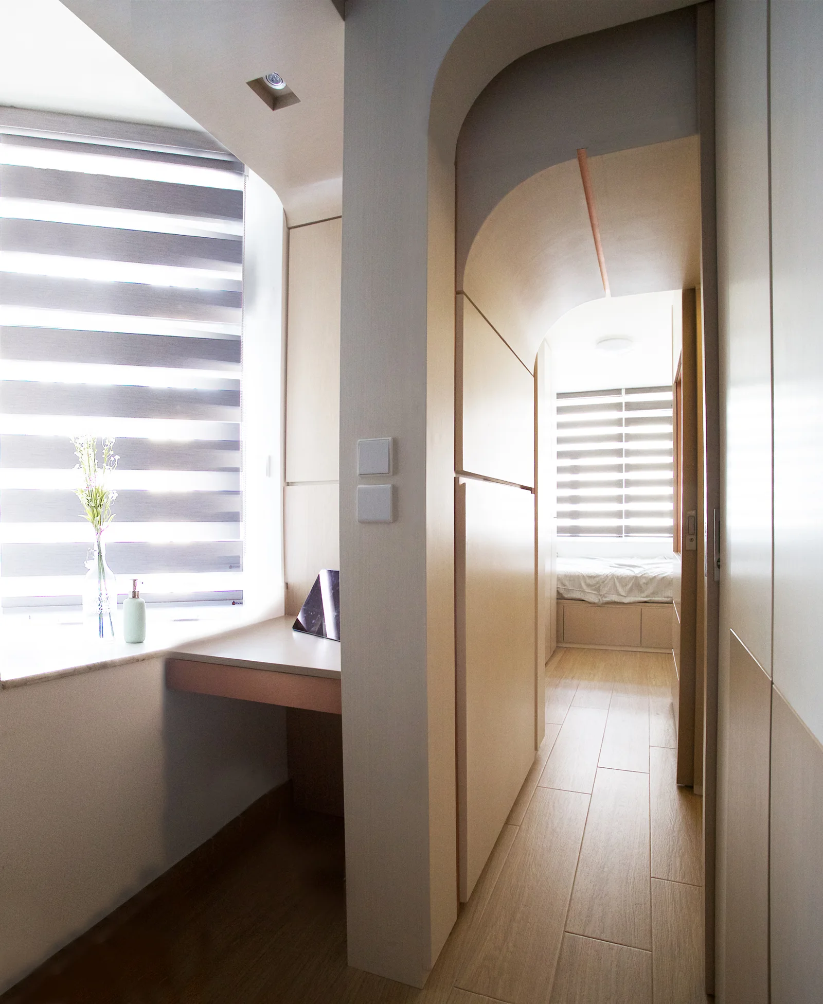 A minimalist built-in desk sits next to a custom curved wood archway that leads into a bedroom.