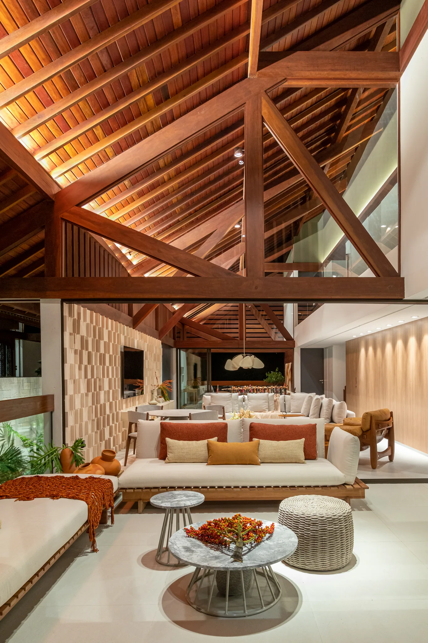 A spacious open-plan living room with a vaulted dark timber truss ceiling, a modern cream sofa, and round marble-topped coffee tables.