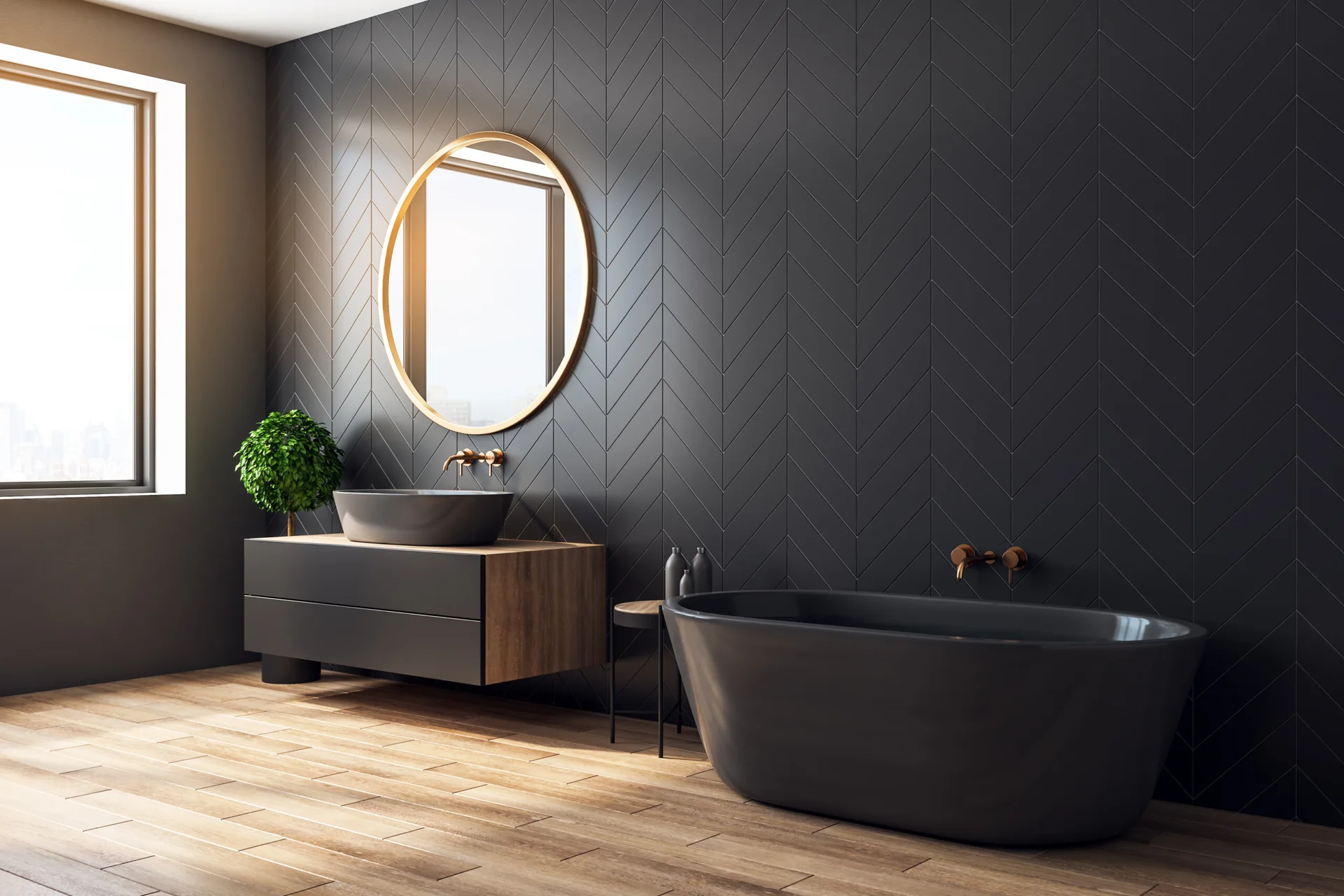 A modern bathroom featuring a dark charcoal herringbone tile wall, a black freestanding bathtub, a wood floating vanity, and a round gold-framed mirror.