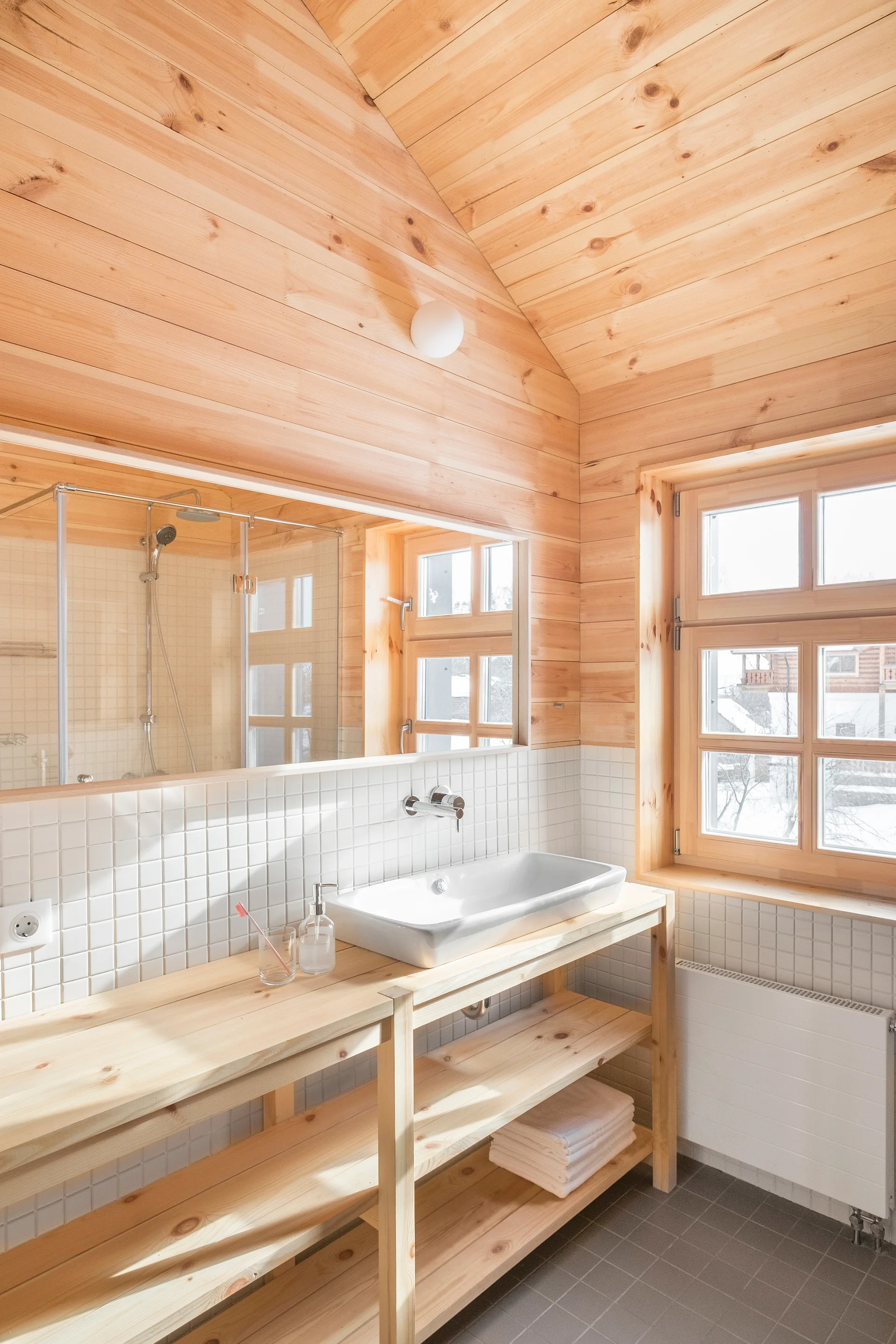 A bathroom with knotty pine paneled walls and ceiling features an open wooden vanity with a white ceramic basin and a large rectangular mirror.