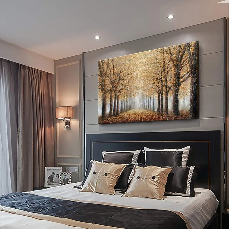 A contemporary bedroom features a large golden forest canvas painting hanging above a dark headboard with patterned accent pillows and grey wall paneling.
