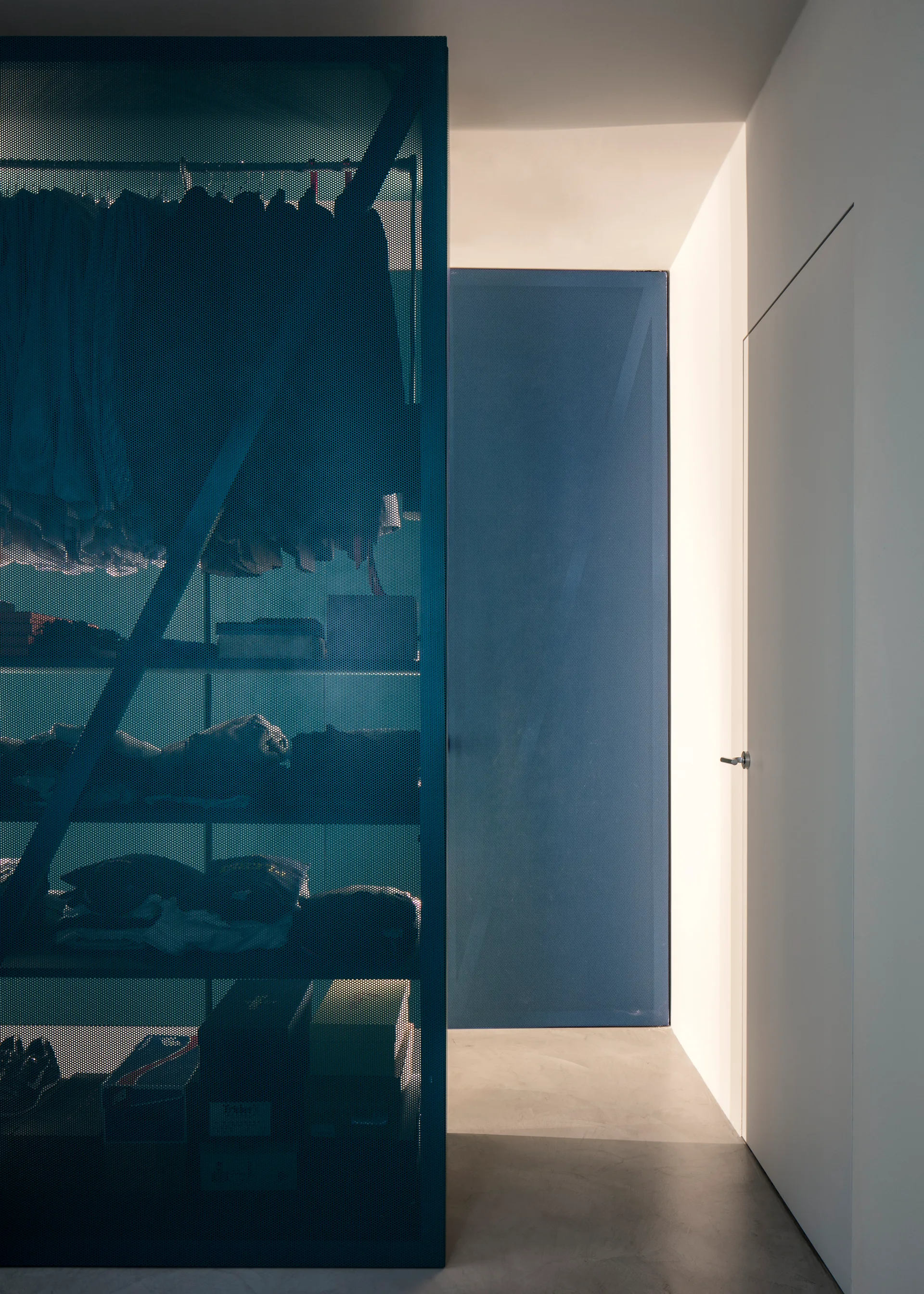 A modern closet features a blue perforated metal screen enclosing a shelving unit next to a smooth concrete floor and white walls.