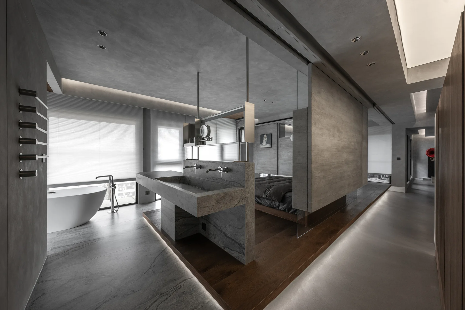 A minimalist open-plan bathroom with a central stone vanity partition, a white freestanding tub, and an elevated wood floor platform.