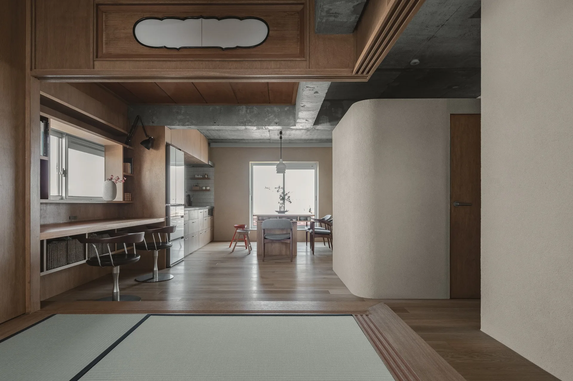 A minimalist interior features a tatami platform in the foreground, wood built-ins, and a curved partition wall under an exposed concrete ceiling.