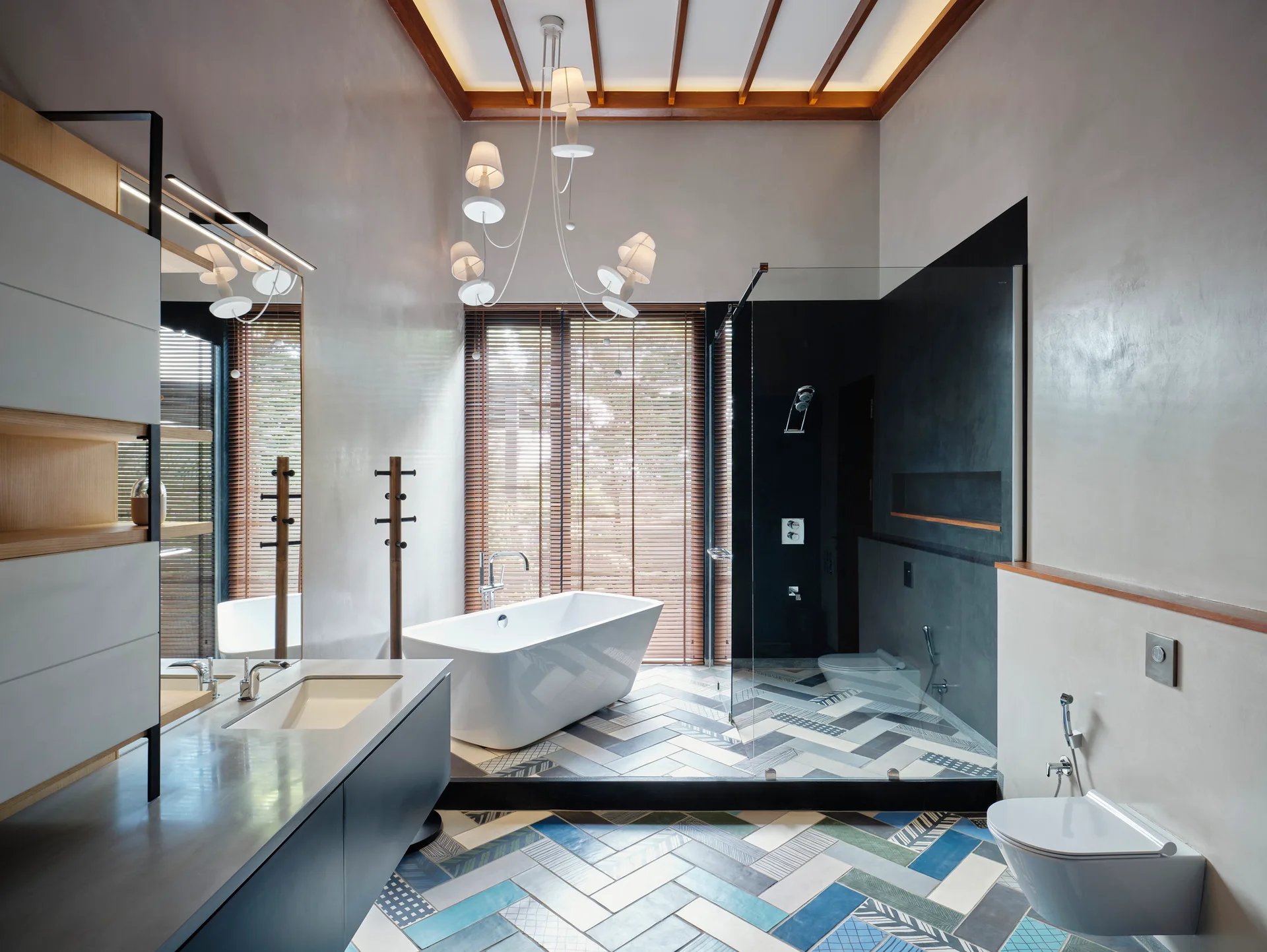A modern bathroom features a white freestanding bathtub, a dark floating vanity, and a blue and grey herringbone patterned tile floor.