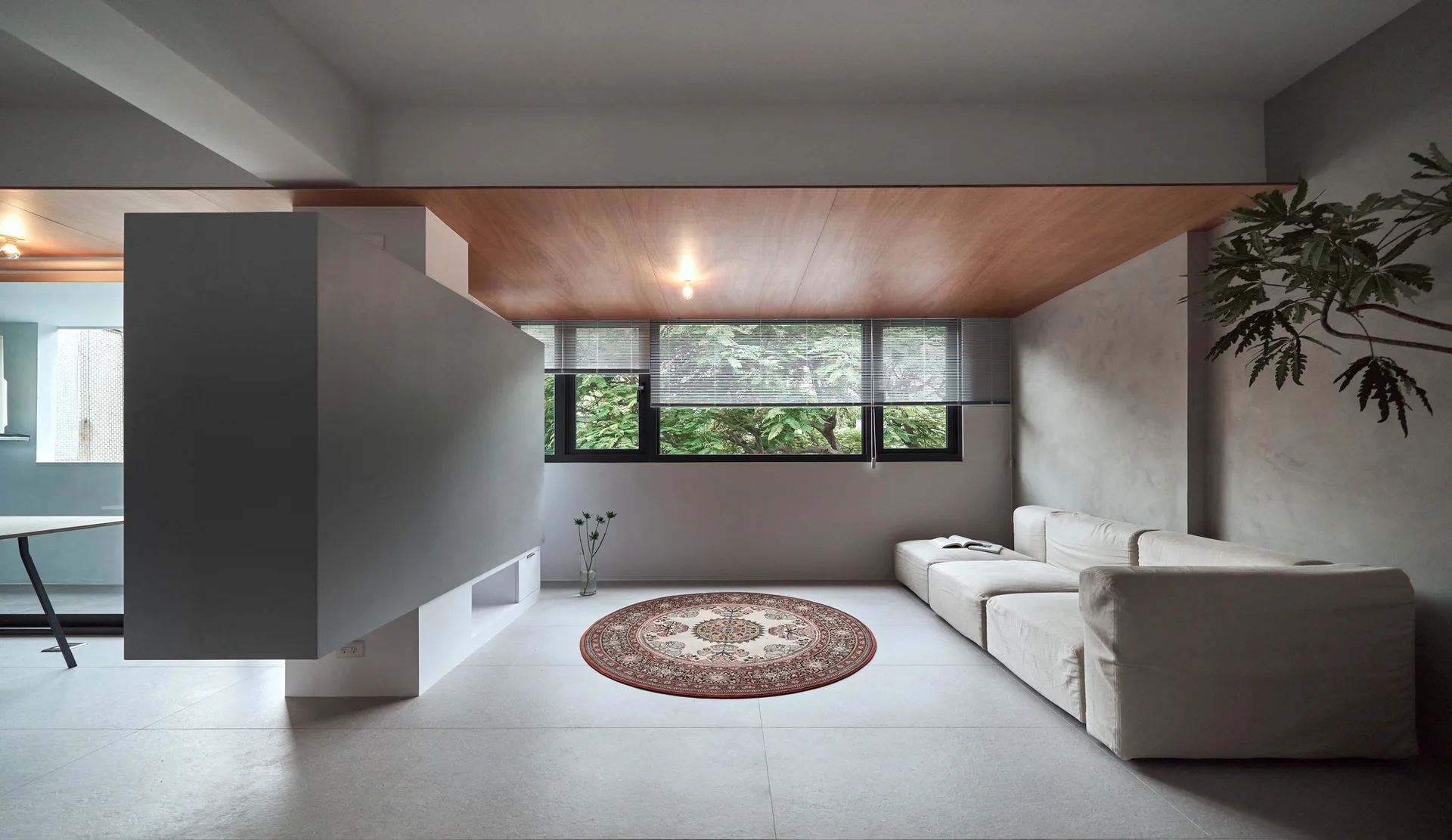 A modern living room features a floating grey partition wall, a cream sofa, a circular ornate rug, and a warm wood-paneled ceiling inlay.