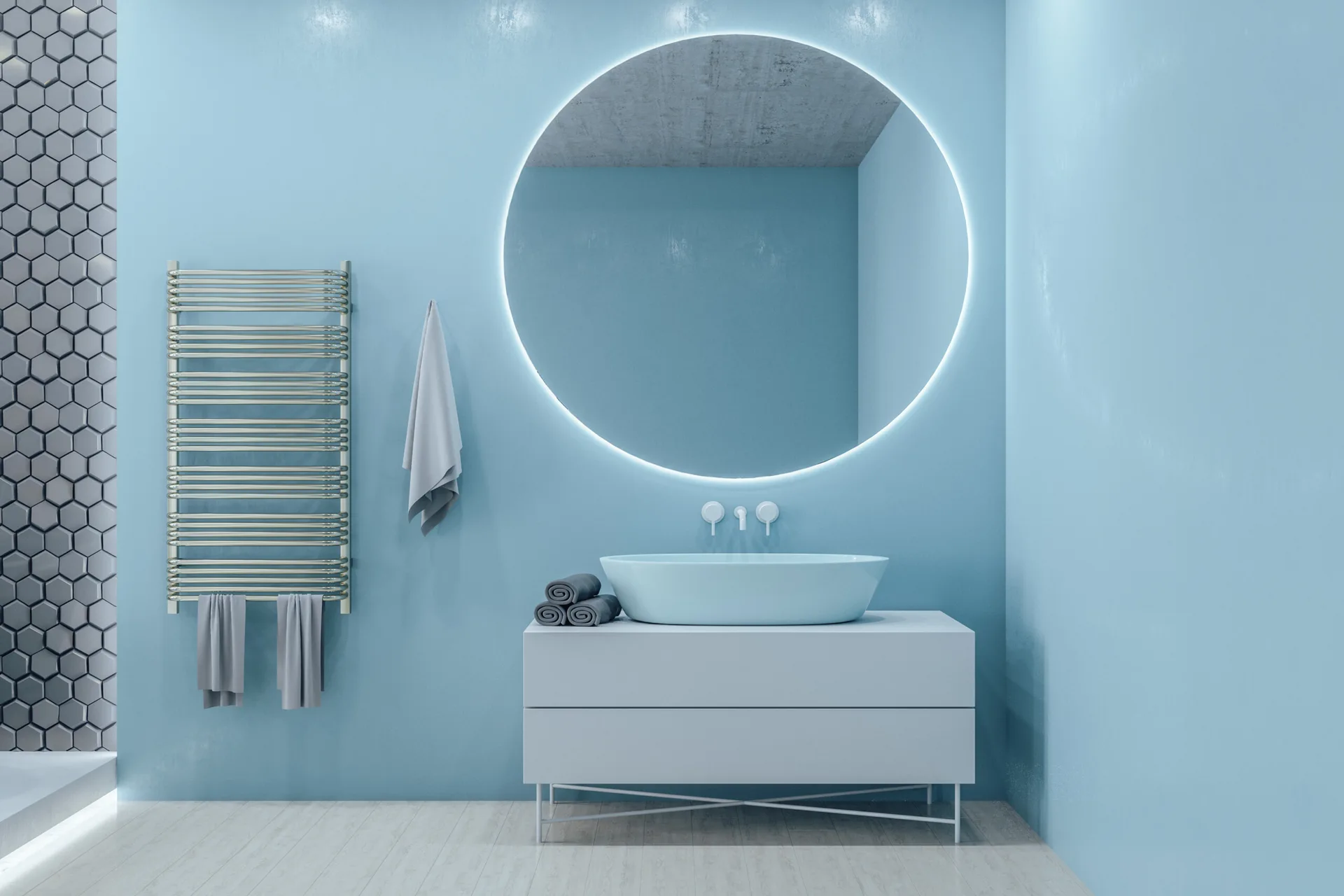 A minimalist bathroom features a light blue wall, a white vanity with a blue vessel sink, a large backlit round mirror, and a chrome towel warmer.