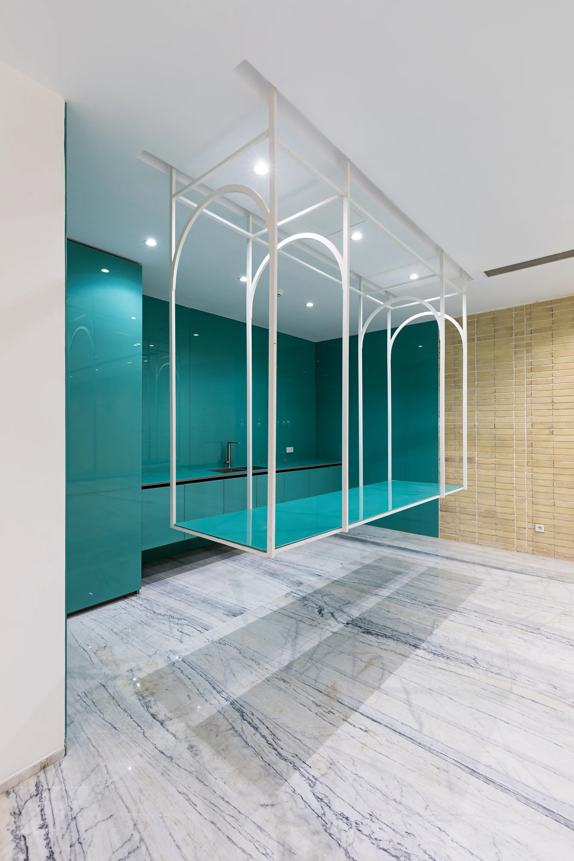 A modern minimalist kitchen with gloss turquoise cabinets, a suspended white metal frame, and polished marble flooring.