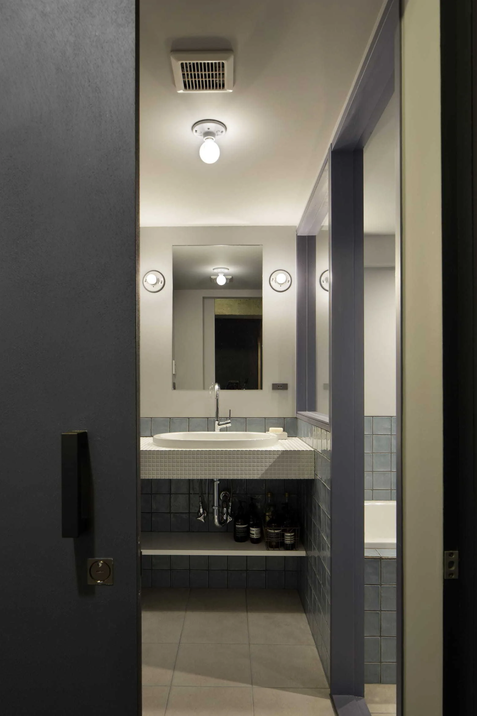 A modern bathroom viewed through a doorway, showing a floating white basin vanity flanked by blue square wall tiles and a rectangular mirror.