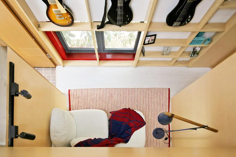 A high-angle view of a wood-paneled reading nook featuring a white armchair, a red striped rug, and built-in shelves displaying guitars.