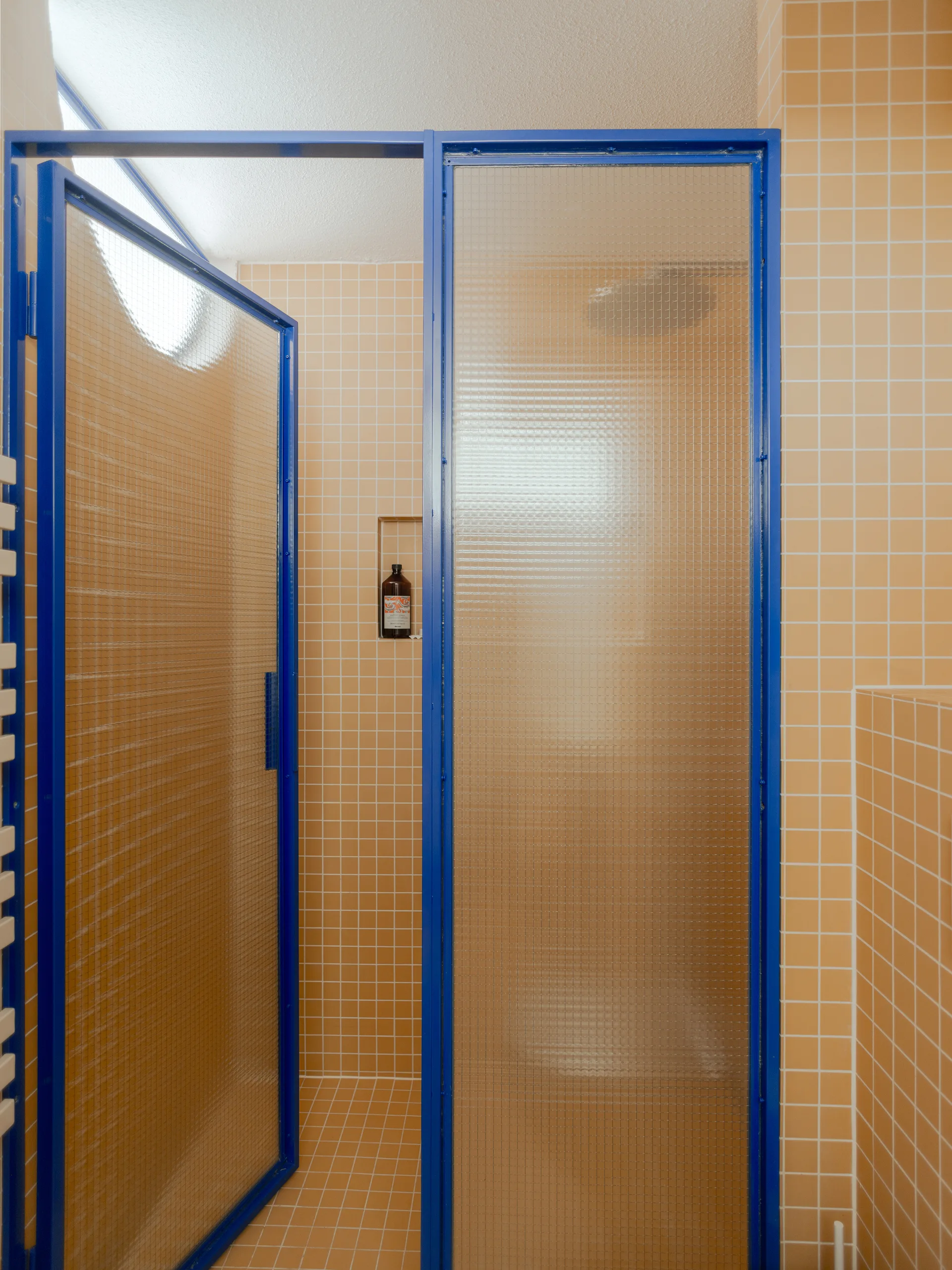 A modern bathroom shower featuring orange square tile walls and textured glass doors in a vibrant blue metal frame.