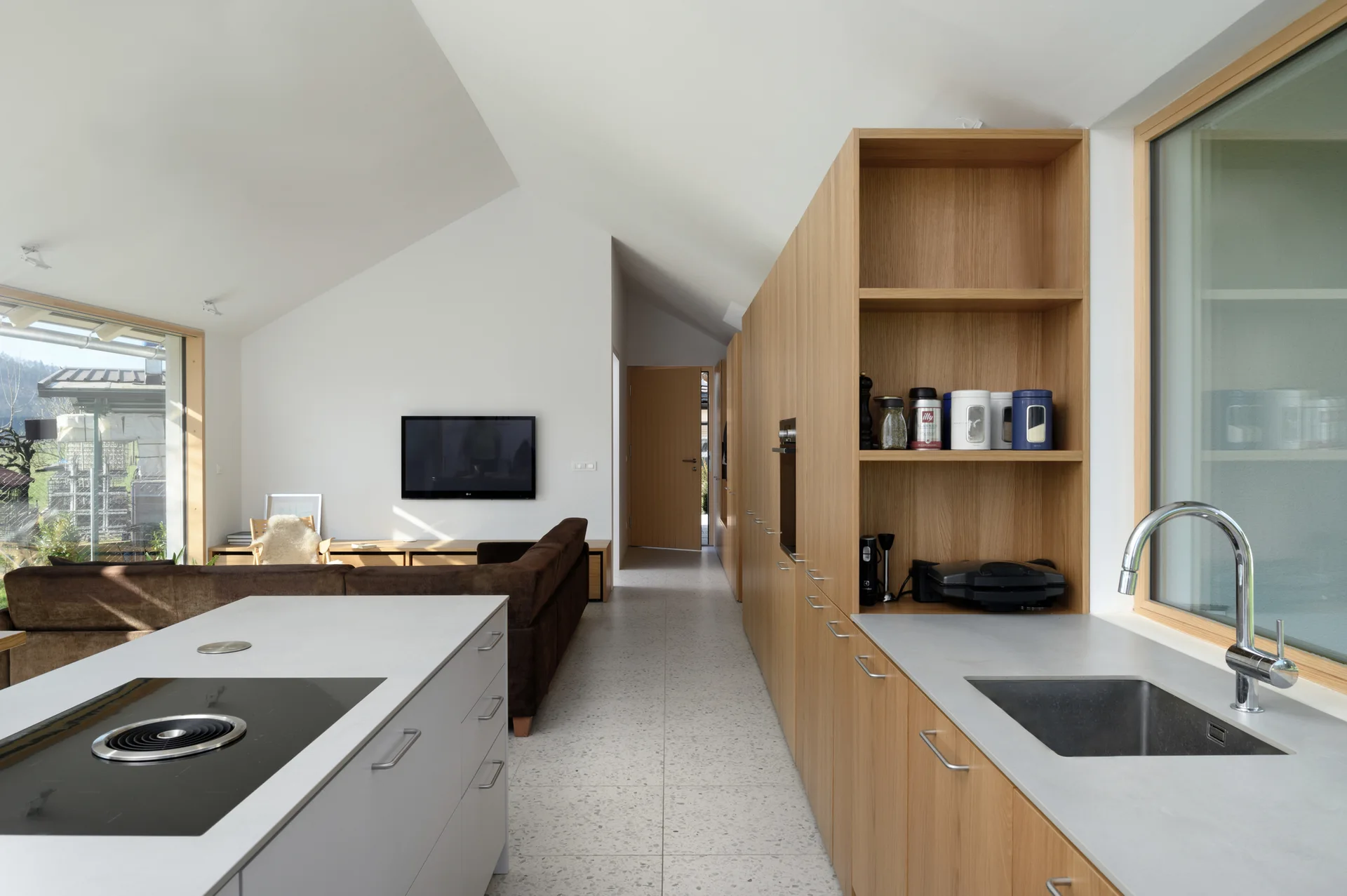 An open-concept kitchen with light oak cabinetry, a grey island, a sink by a window, and a vaulted ceiling leading into a living area.