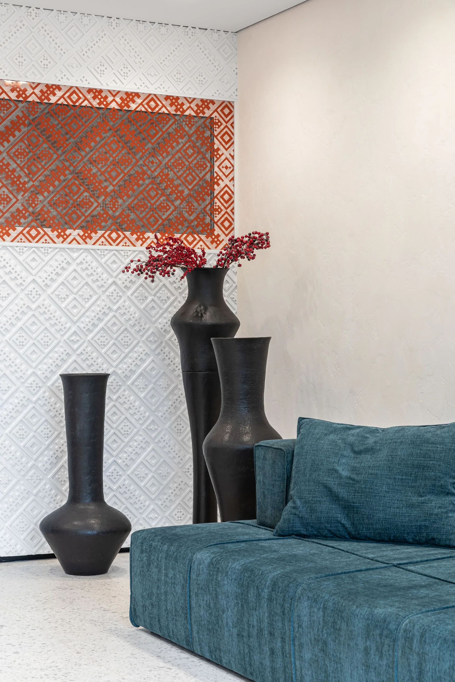 Teal fabric sofa in a modern living room next to three tall black floor vases and an embossed white geometric wall panel.