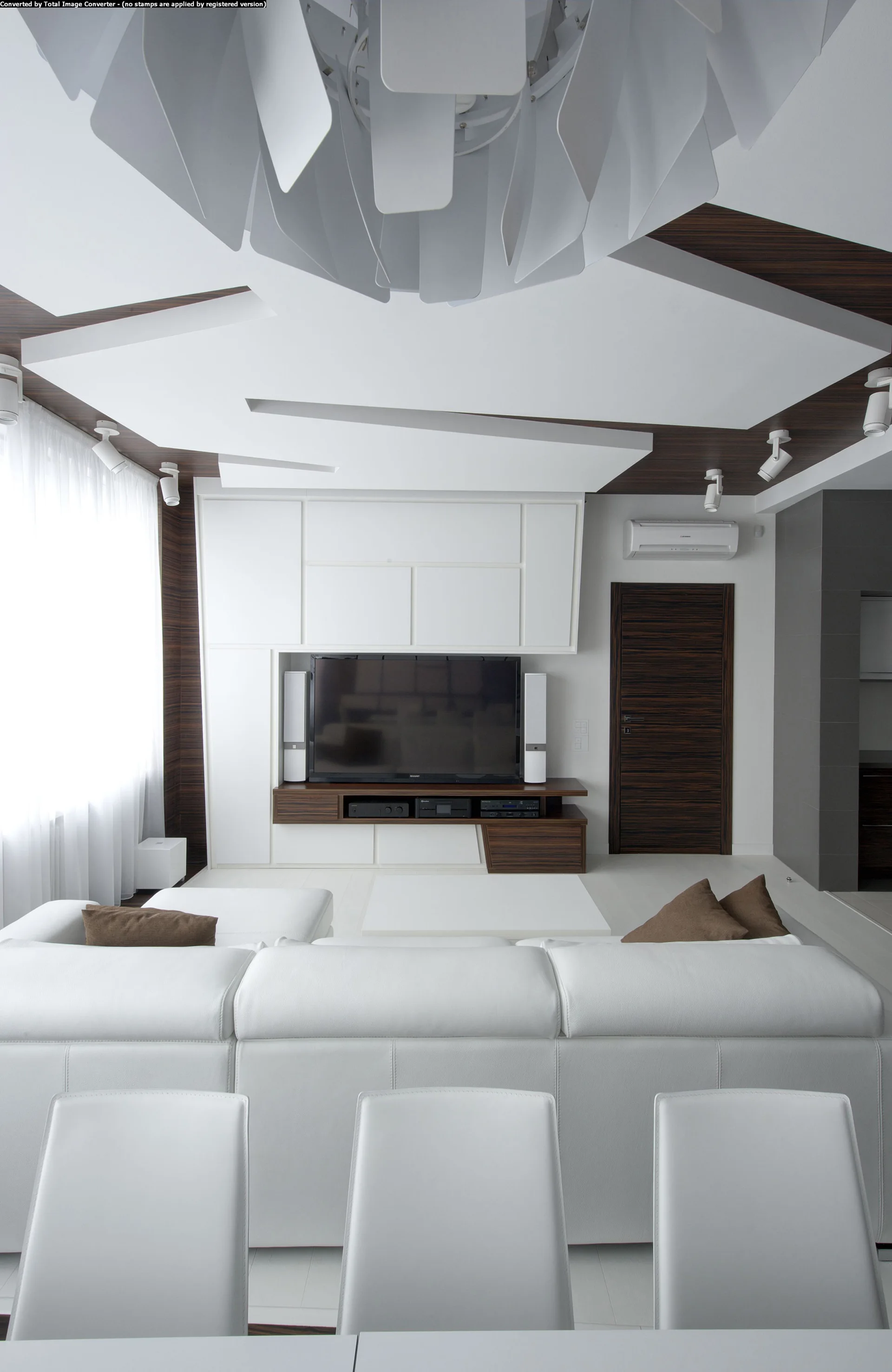 A modern living room featuring a white leather sofa, a custom geometric ceiling with wood accents, and a built-in media unit with a television.