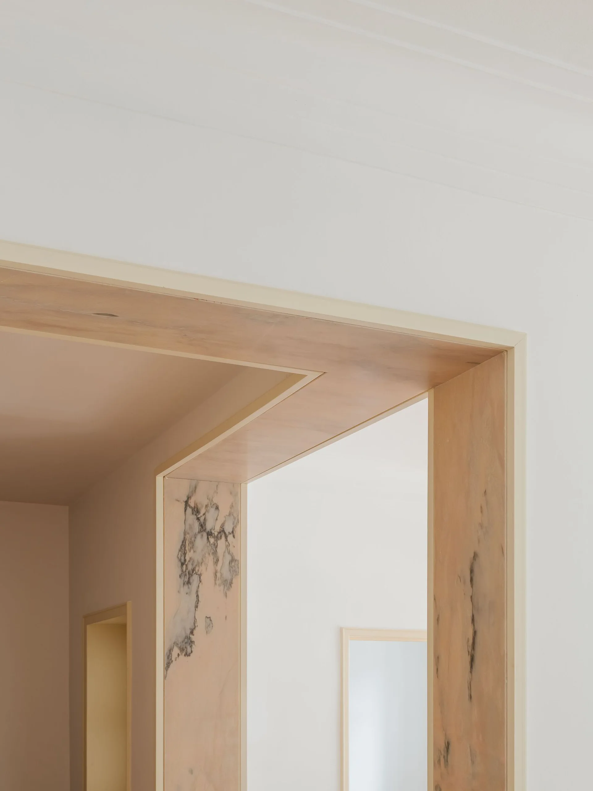 A close-up of a minimalist doorway featuring a multi-layered frame crafted from warm wood and polished veined marble against white walls.