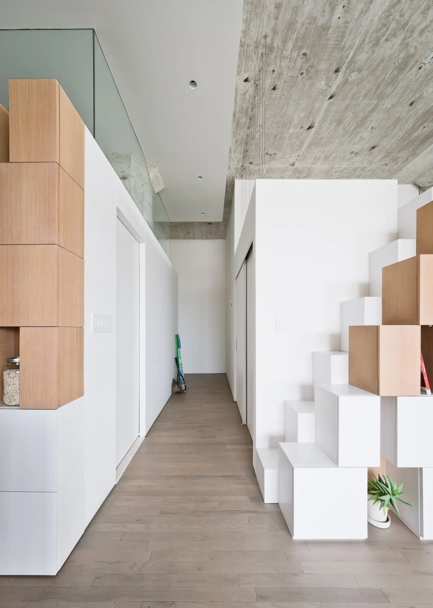 A minimalist hallway featuring a modular staircase made of white and light wood blocks under an exposed concrete ceiling.
