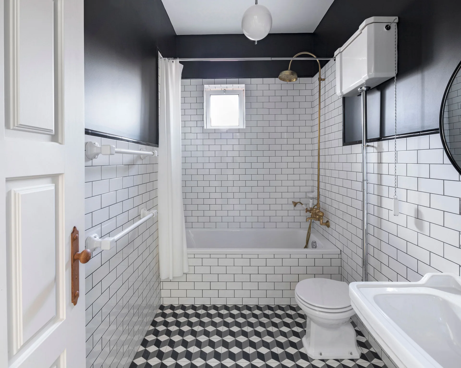 A black and white bathroom featuring white subway tiled walls, a high-tank toilet, brass shower fixtures, and geometric cube-patterned floor tiles.
